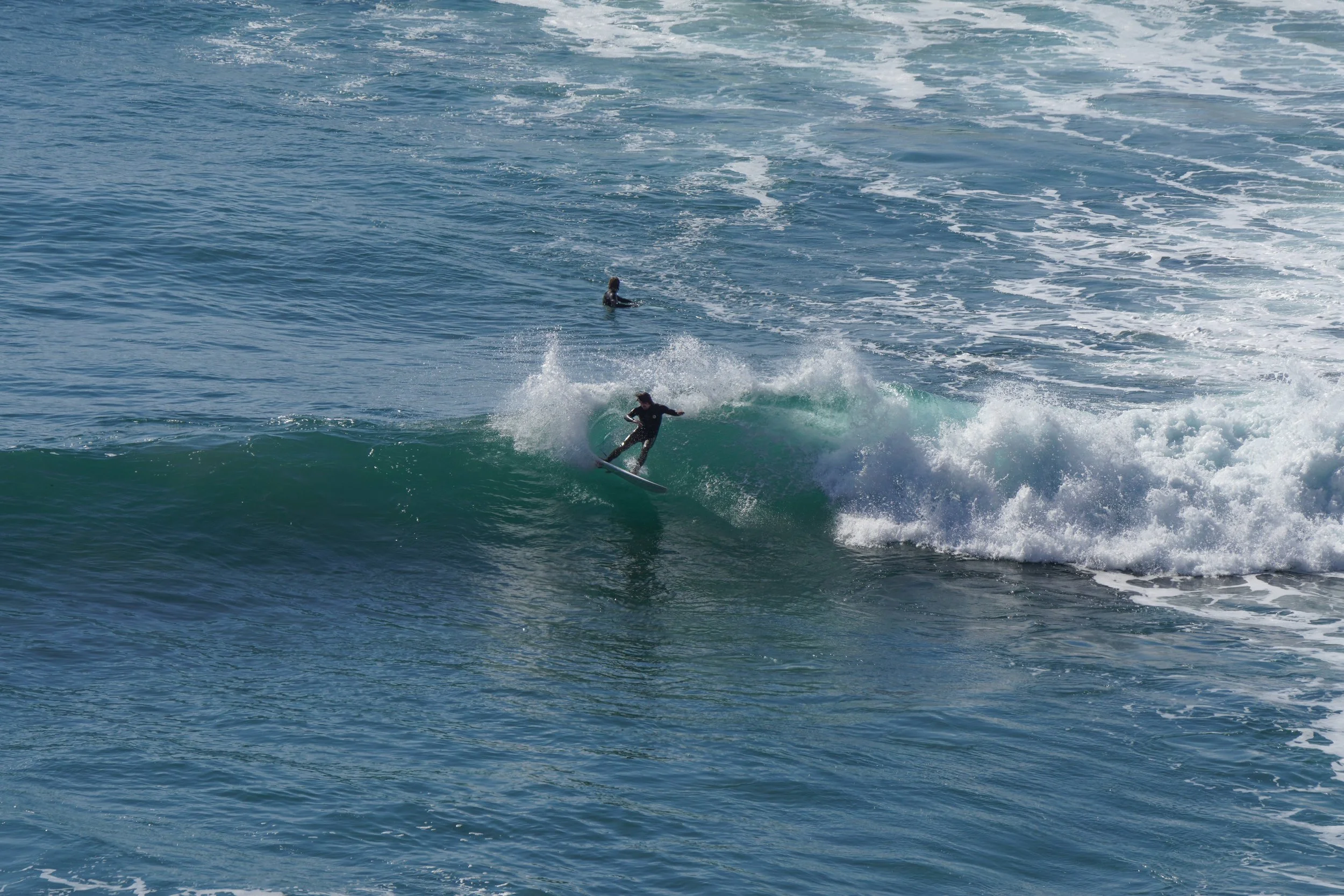A person surfing on a wave in the ocean with another person in the background.