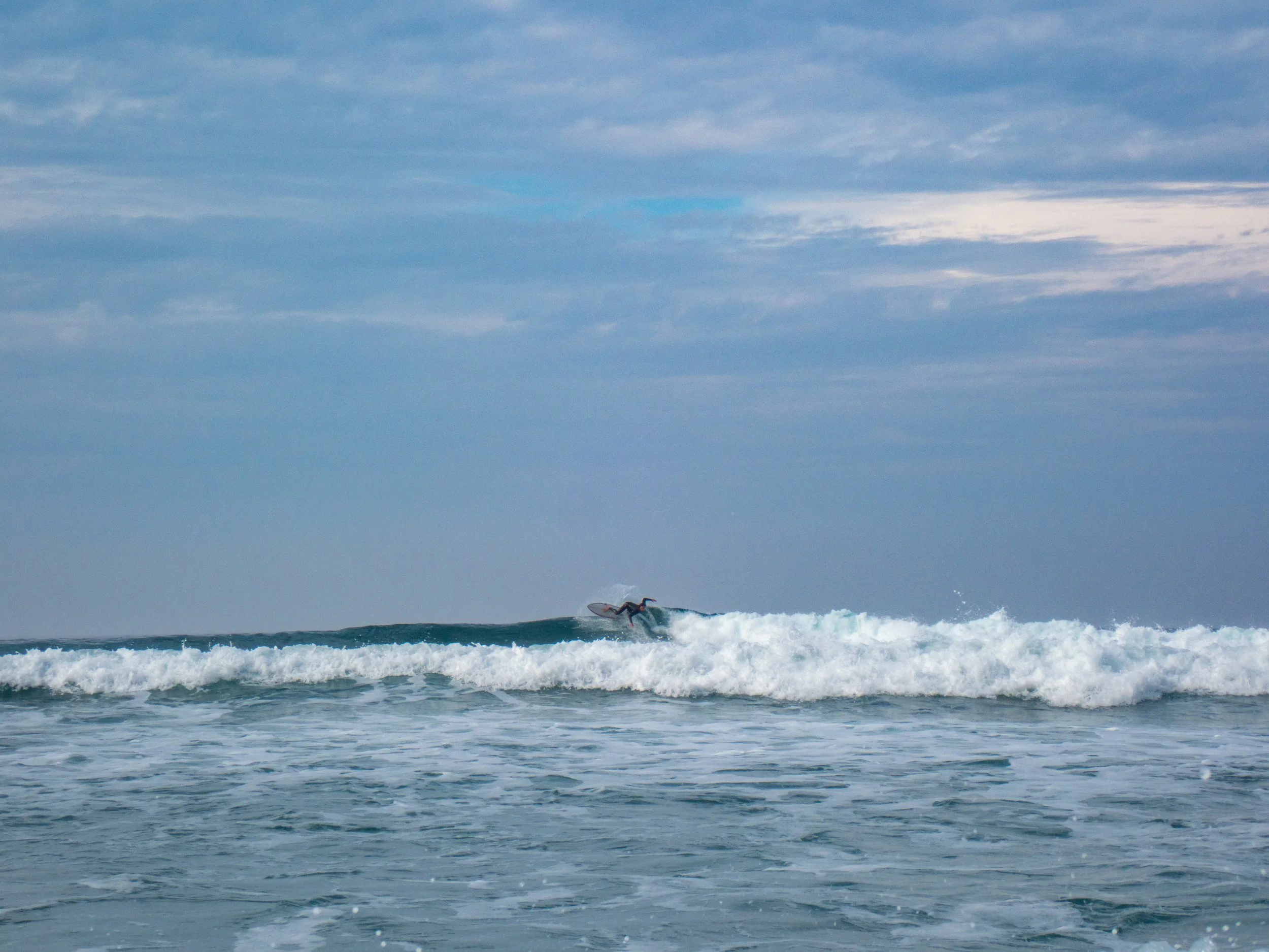 A person surfing on a wave in the ocean under a partly cloudy sky.