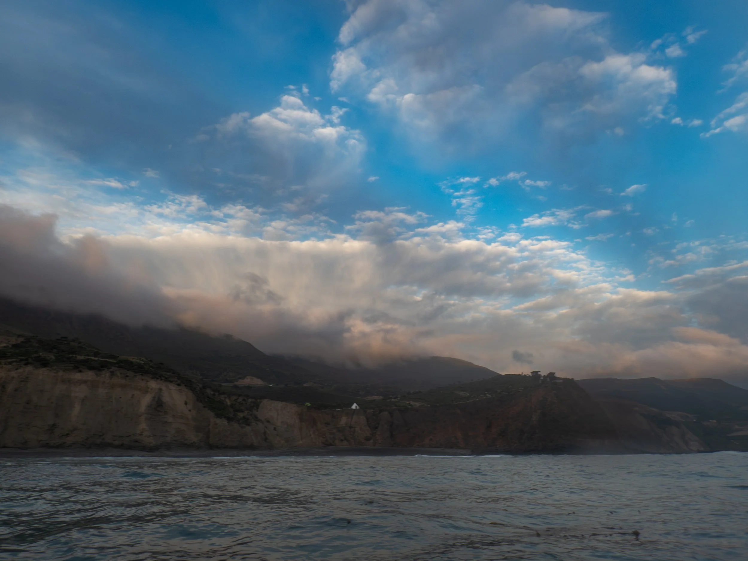 A coastal landscape with cliffs, ocean, and a sky filled with clouds.
