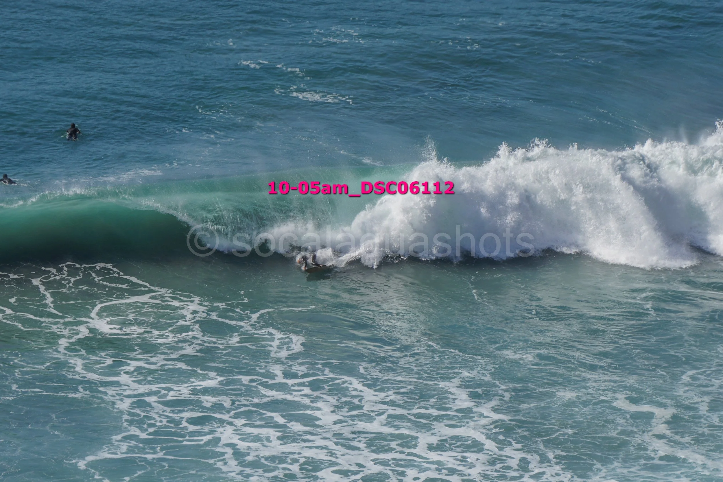 A surfer riding a wave with two other surfers visible in the background in the ocean.
