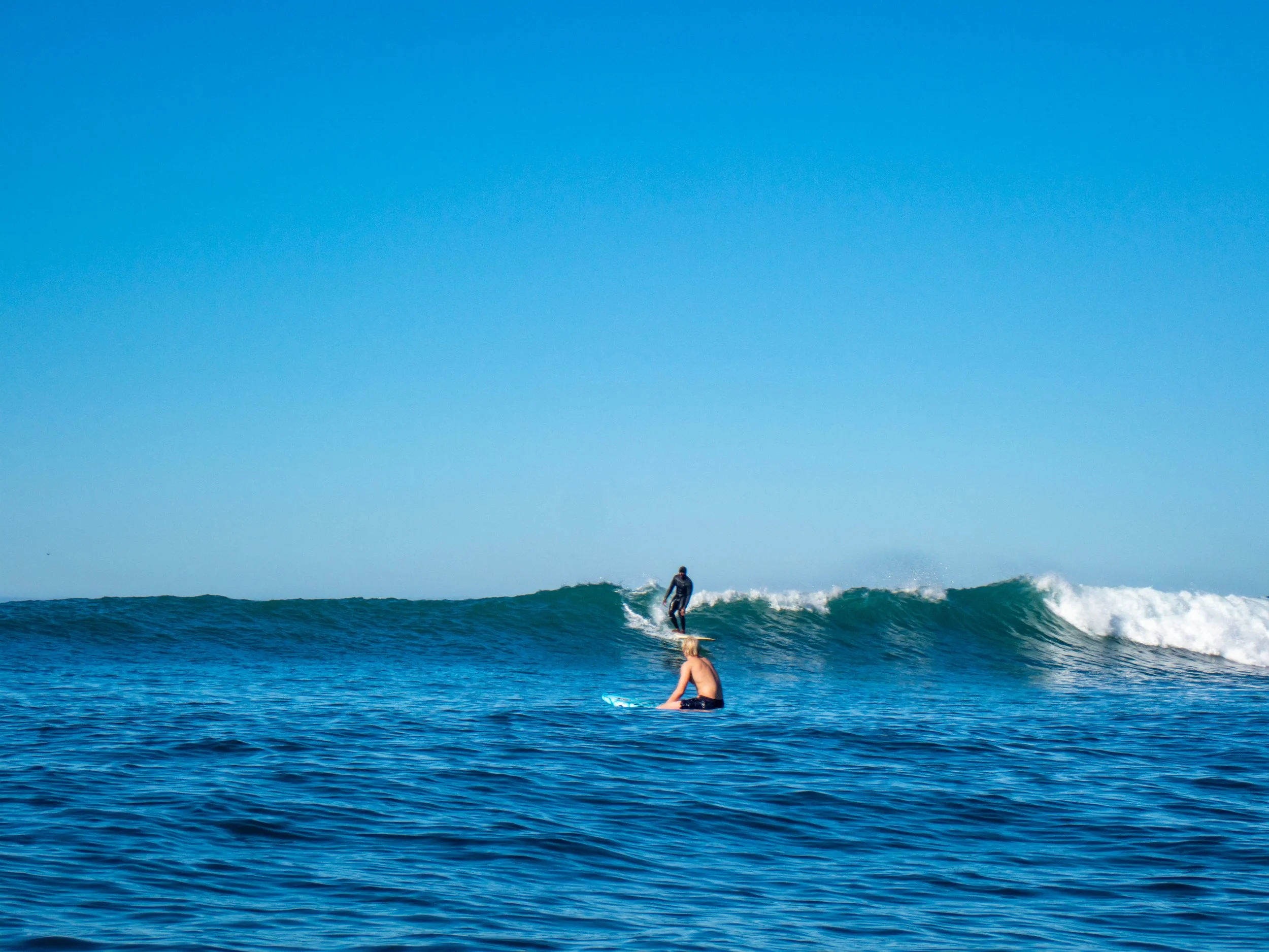 Person surfing on a wave in the ocean with a clear blue sky overhead.