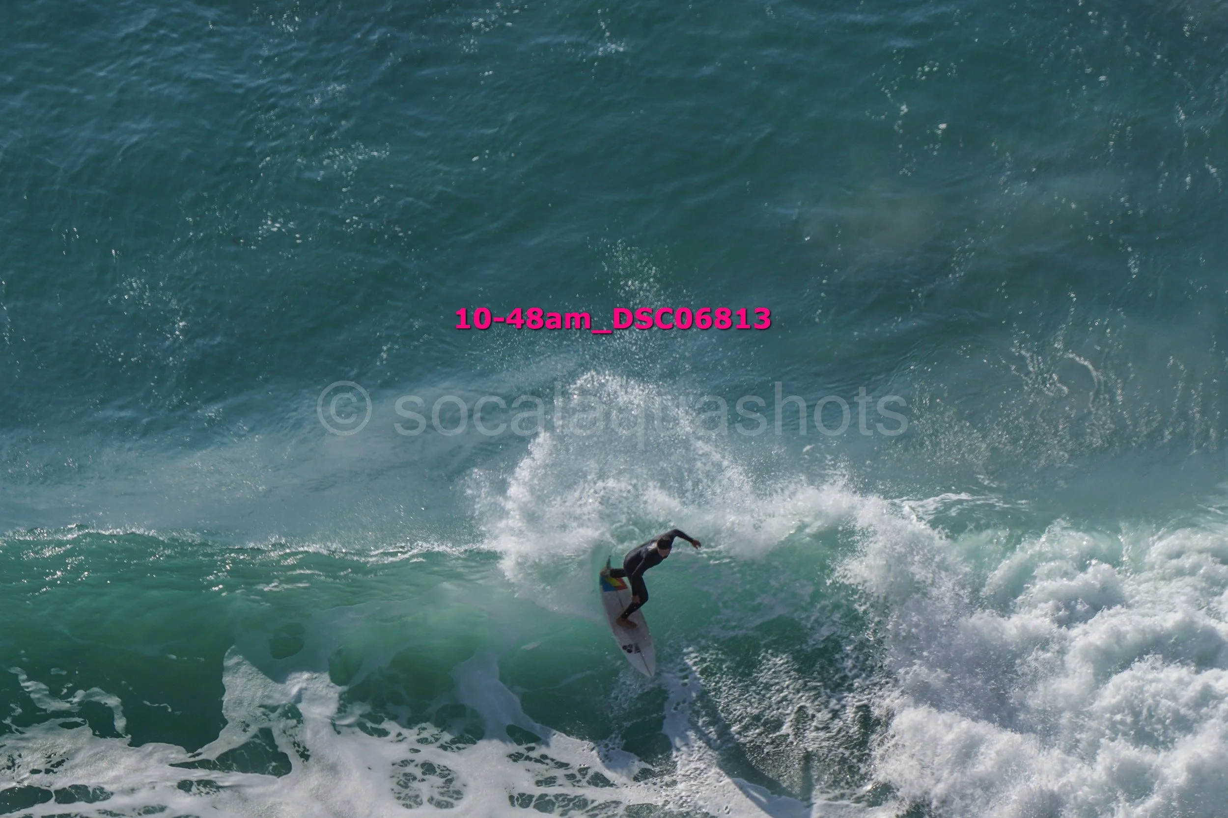 Surfer riding a wave in the ocean, with spray and foam, under a blue sky.