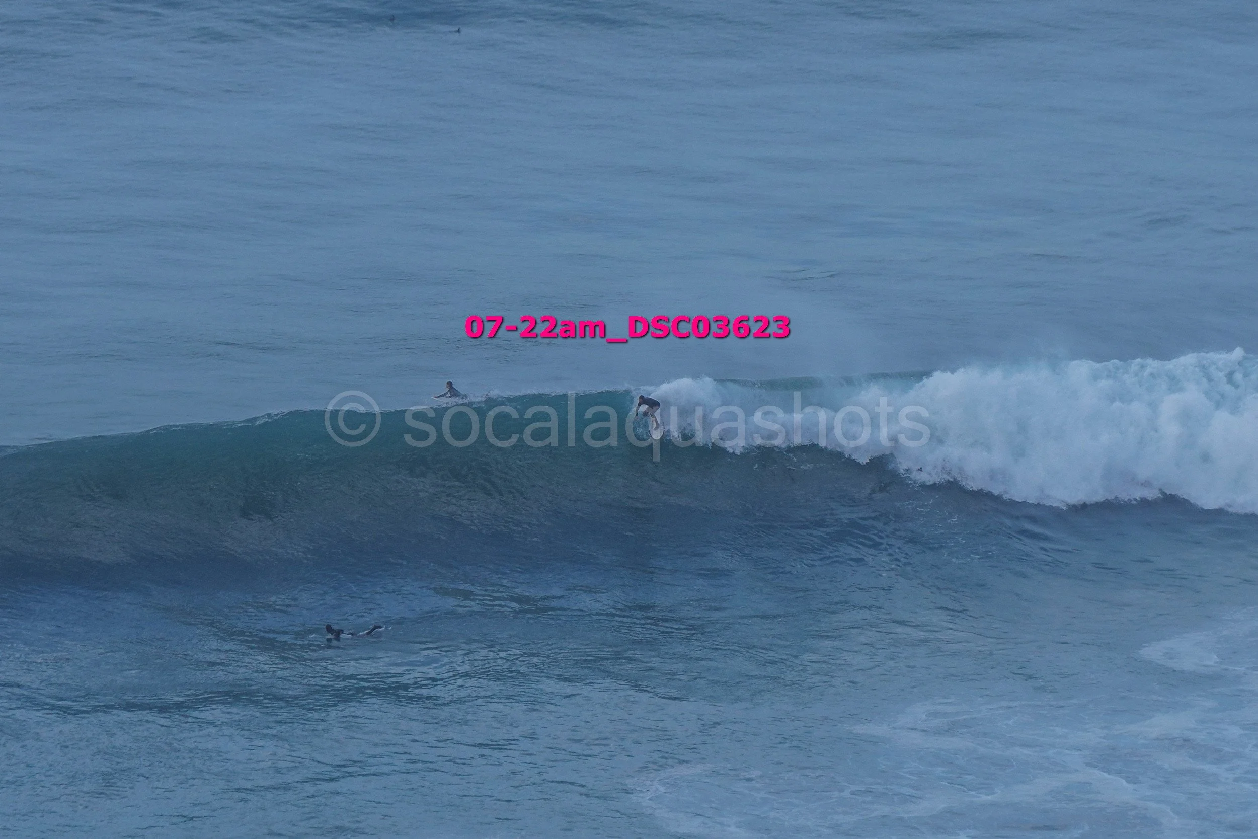 Surfers riding waves in the ocean at dawn.