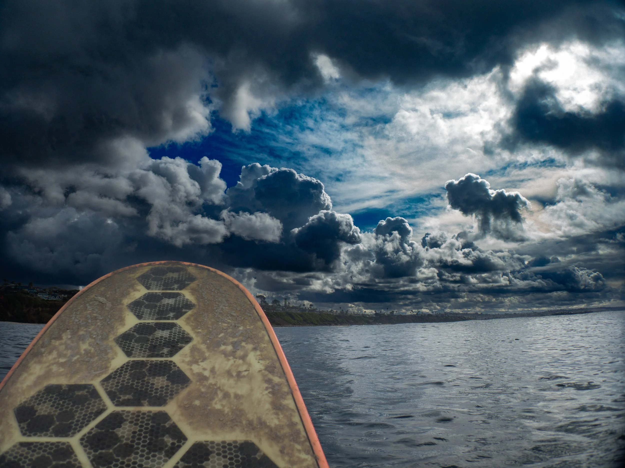 The photo shows a view from a paddleboard on a body of water under a cloudy sky with dark storm clouds and some blue sky visible.