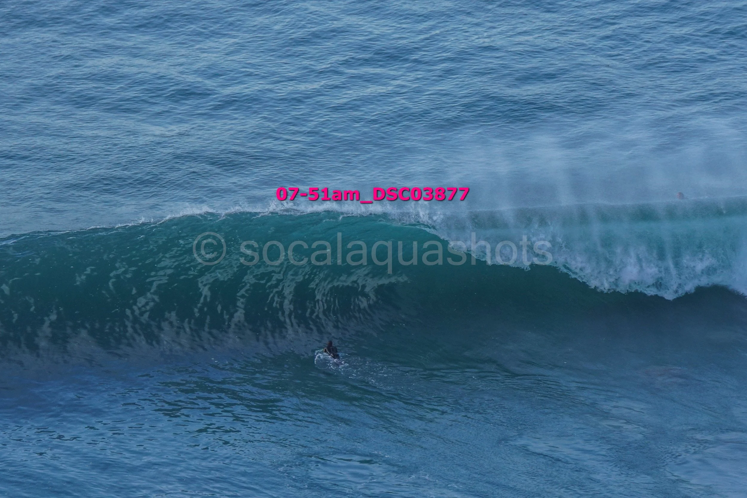 A person surfing on a large ocean wave with water spray in the background.