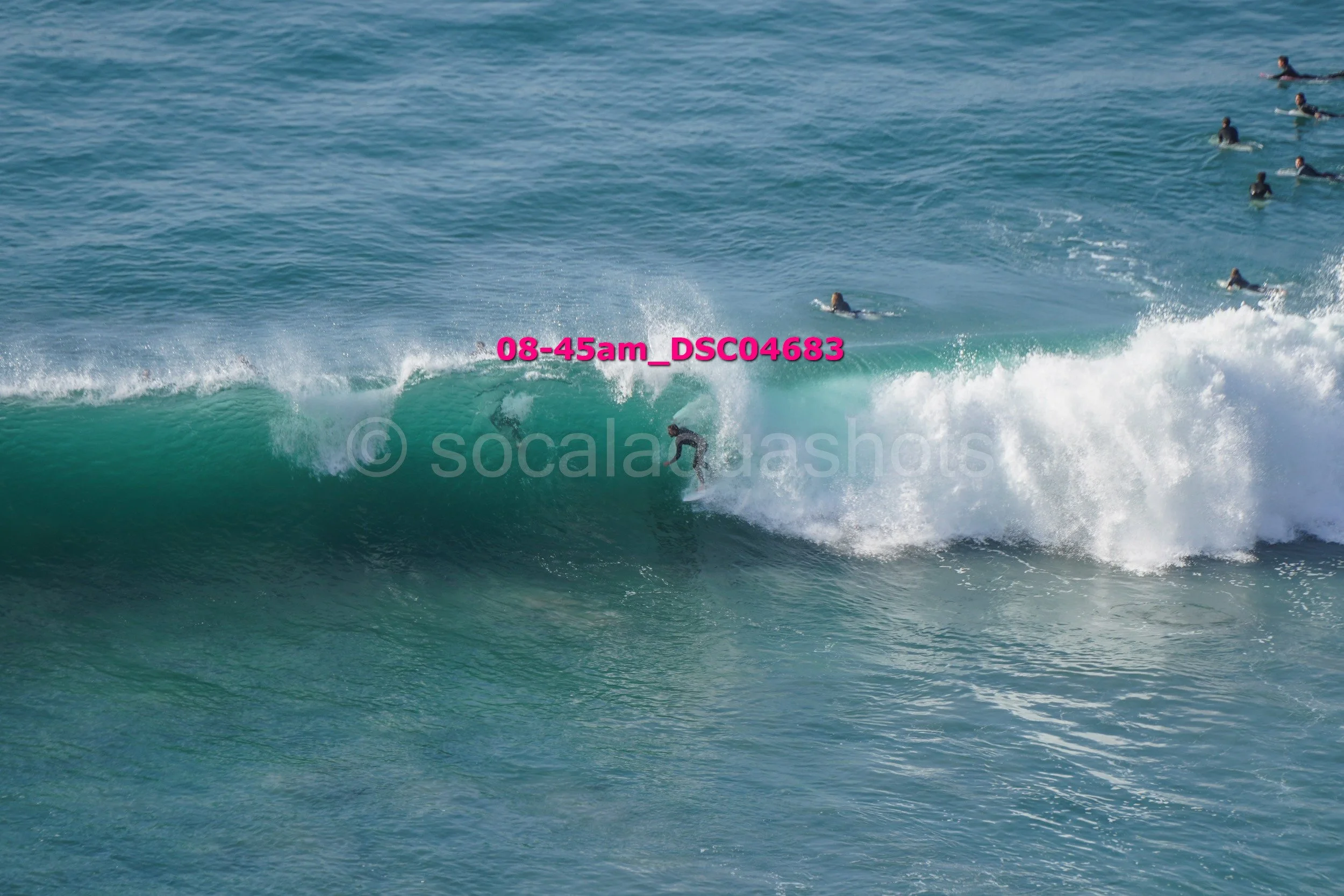 A surfer riding a wave in the ocean with several people in the water watching from behind.