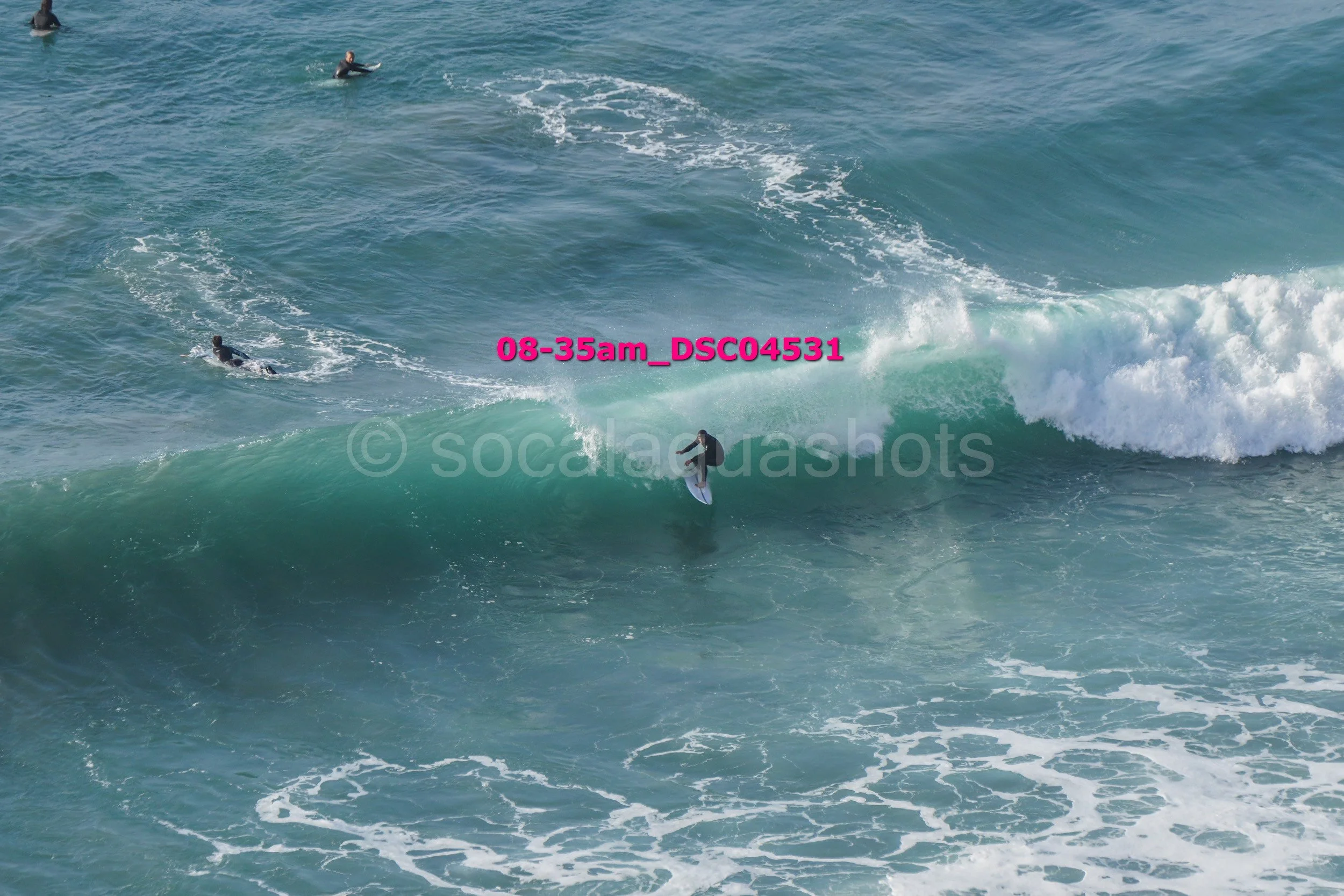 A person surfing on a wave with three other surfers in the water nearby.