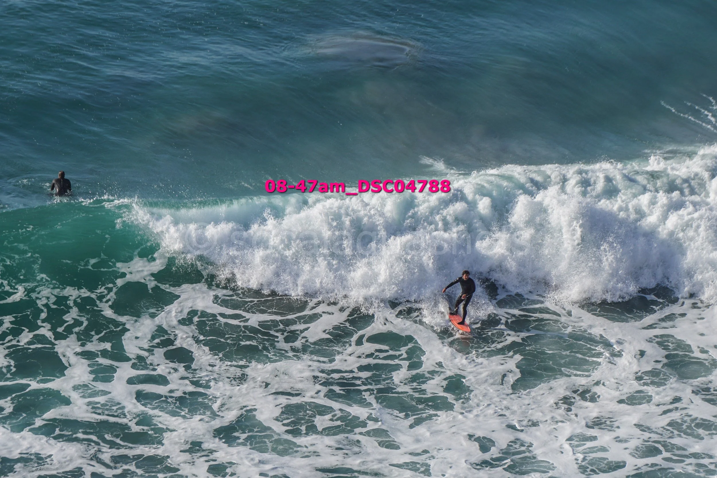A person surfing on a wave in the ocean, with another person in the water nearby.