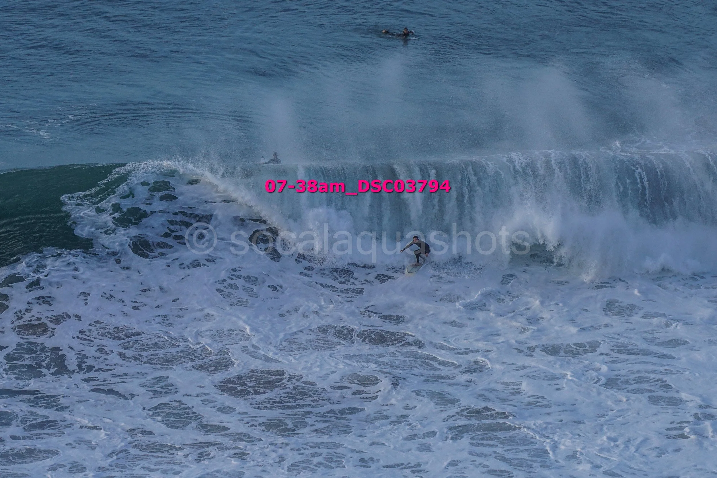 Surfer riding a wave in the ocean with a person swimming in the background.