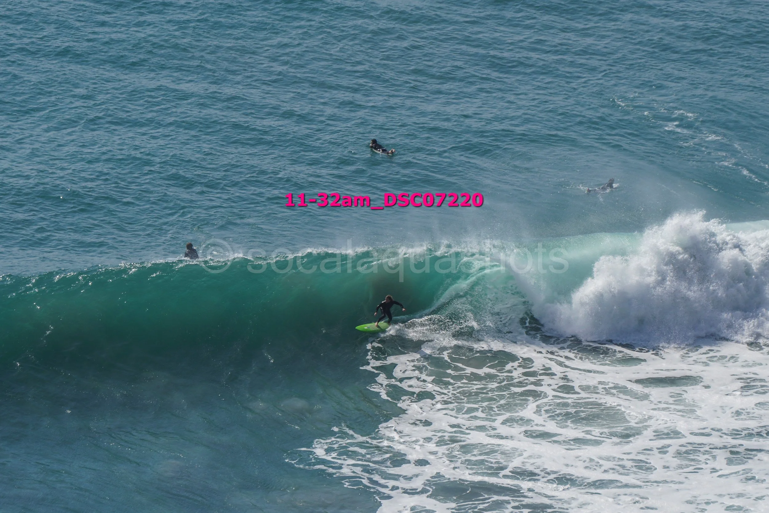 A person surfing on a large wave in the ocean with three other people in the water nearby.
