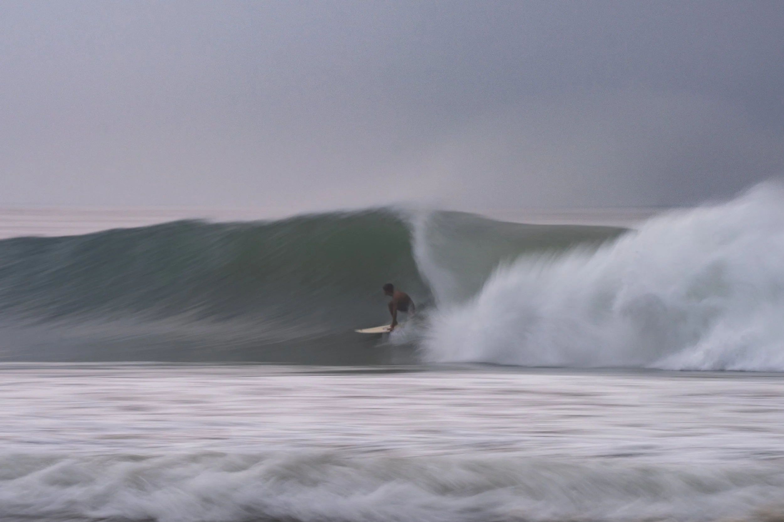 A person surfing on a wave in the ocean with a cloudy sky overhead.