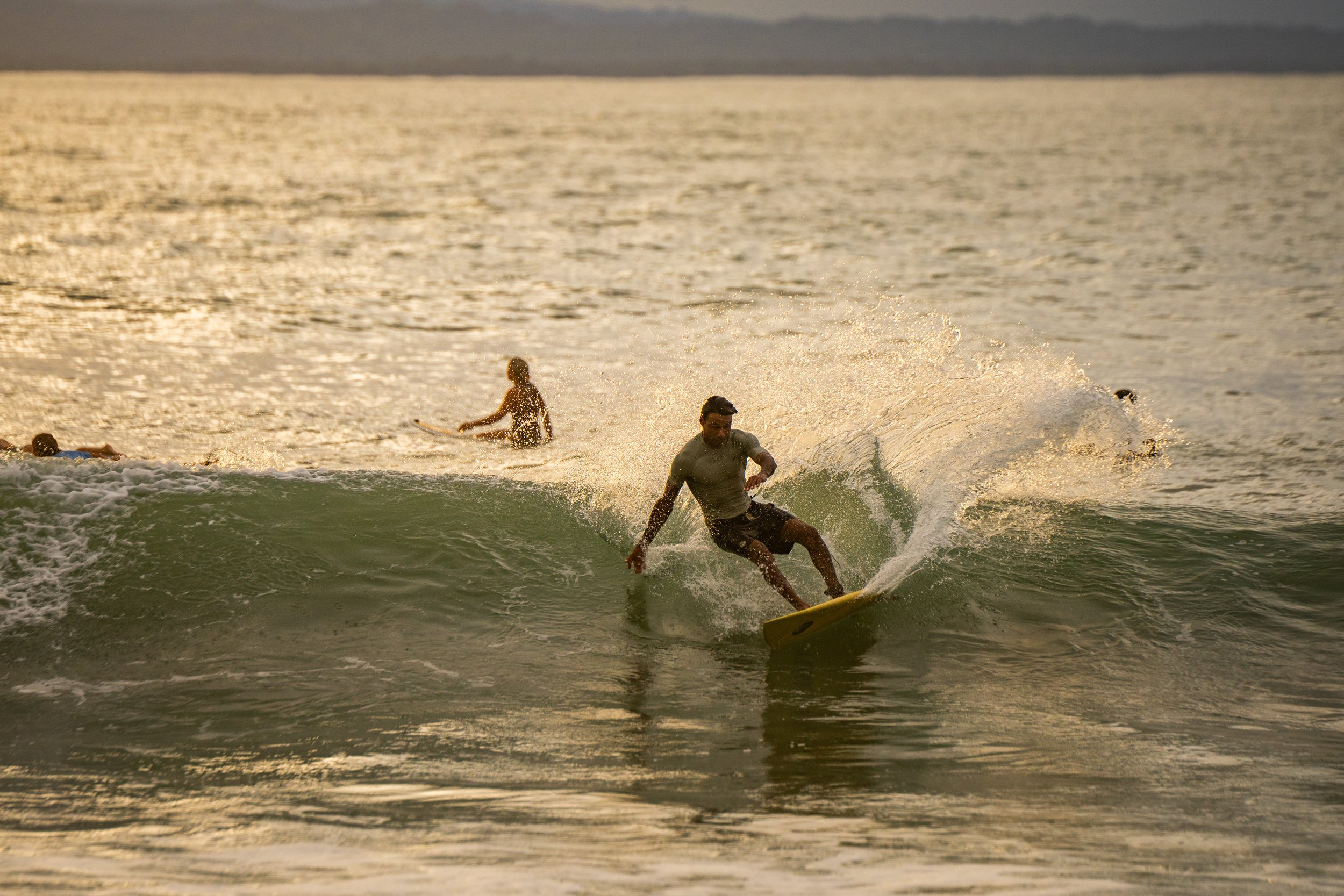 A person surfing on a wave during sunset with other surfers in the background.