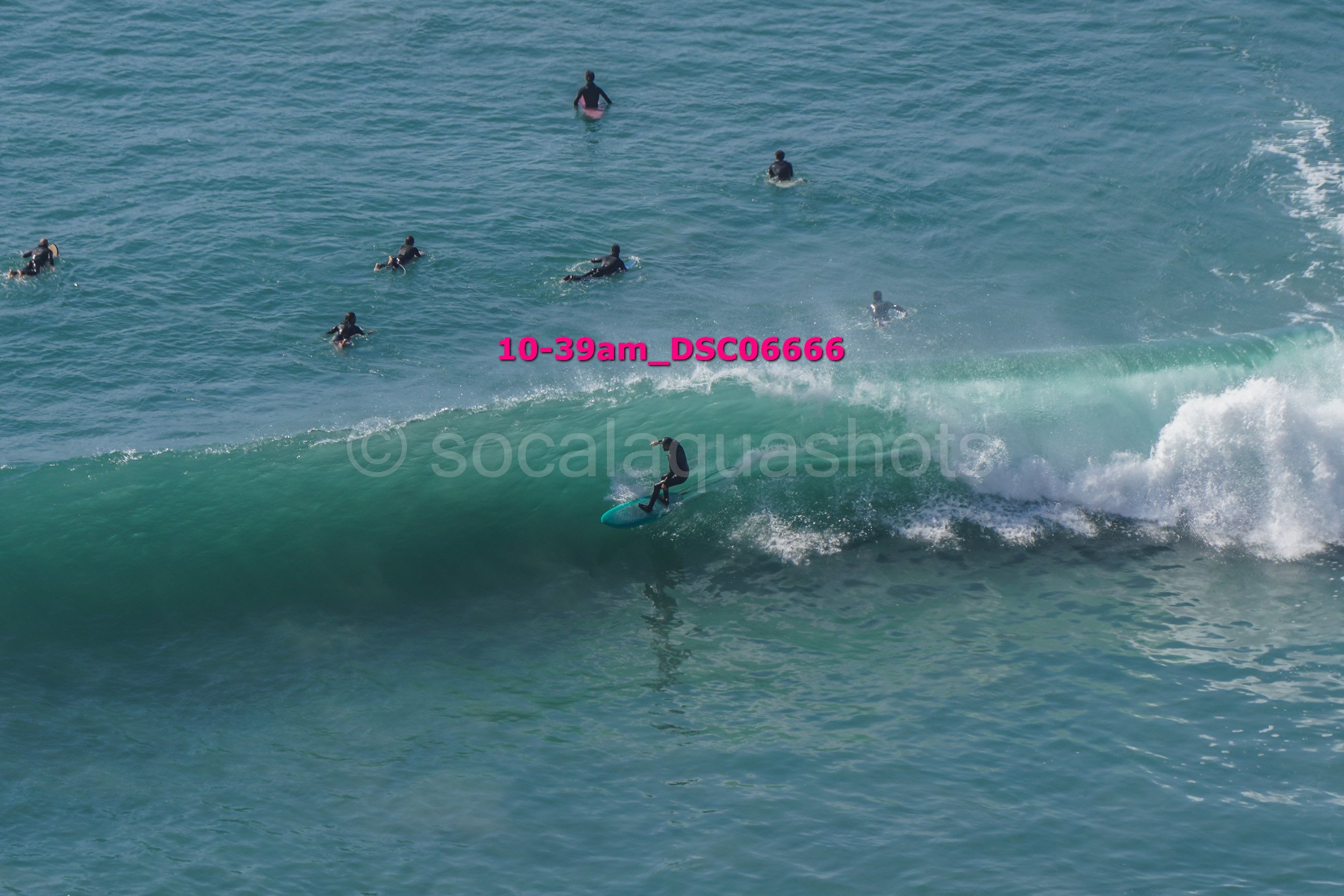A surfboarder riding a wave with several surfers in the water in the background.
