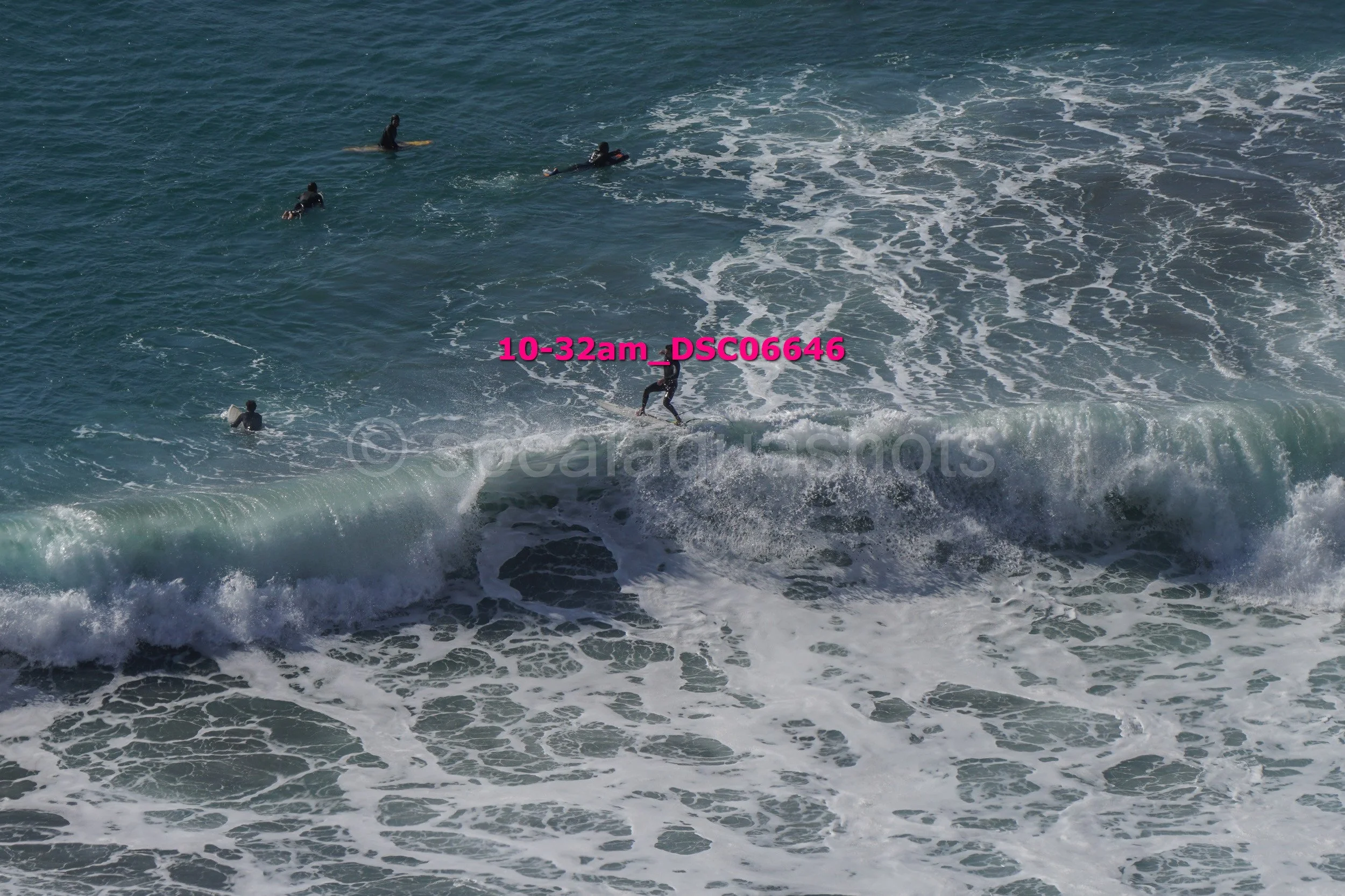 Surfer riding a wave with several other surfers in the water nearby on a sunny day at the beach.