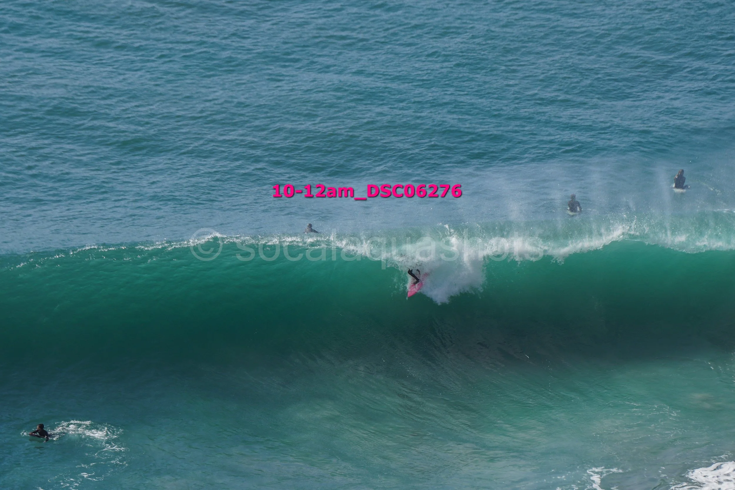 A surfer rides a large wave with several water surfers in the background in the ocean.