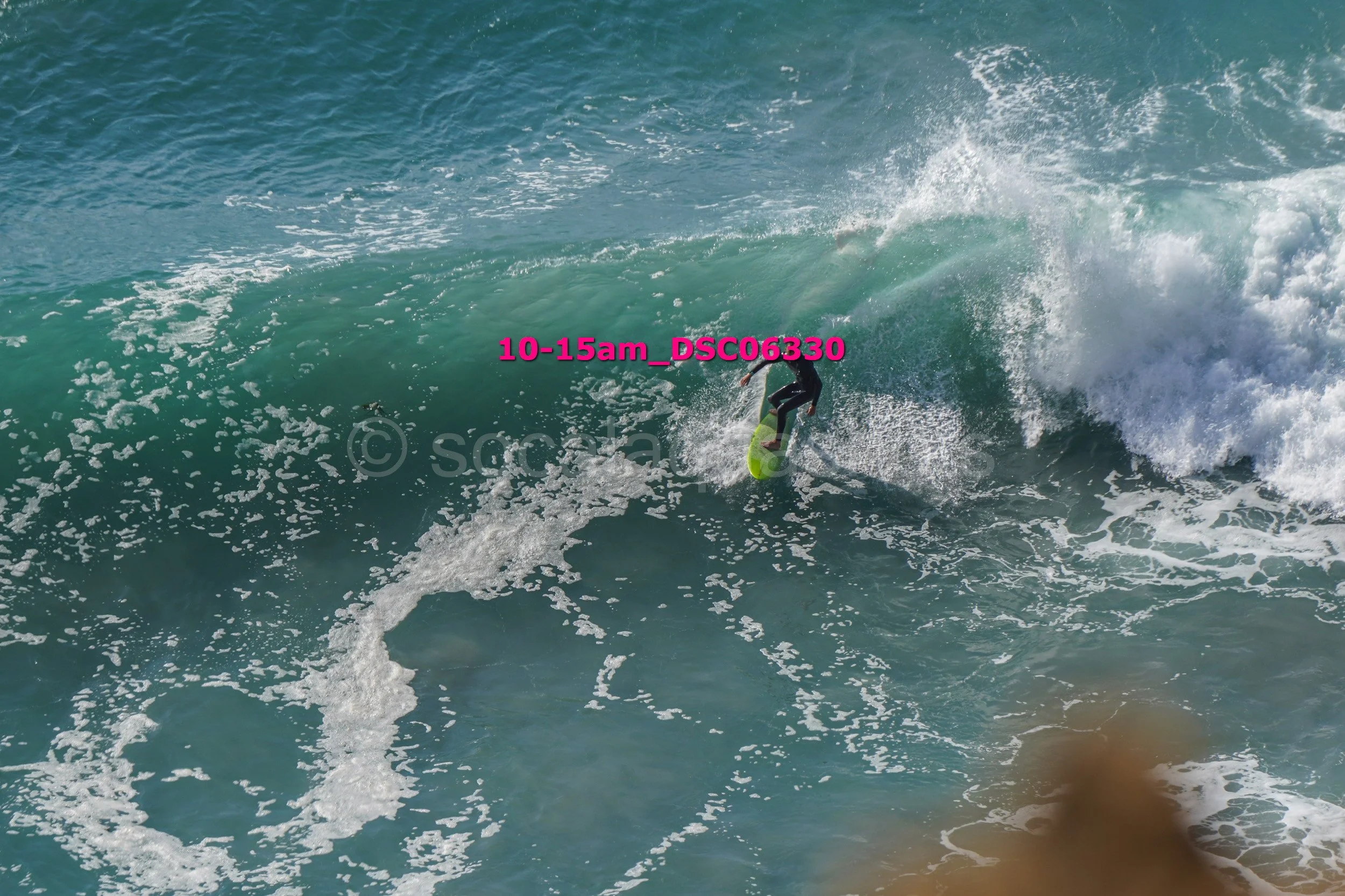 A person surfing on a large ocean wave with a green surfboard, wearing a wetsuit.