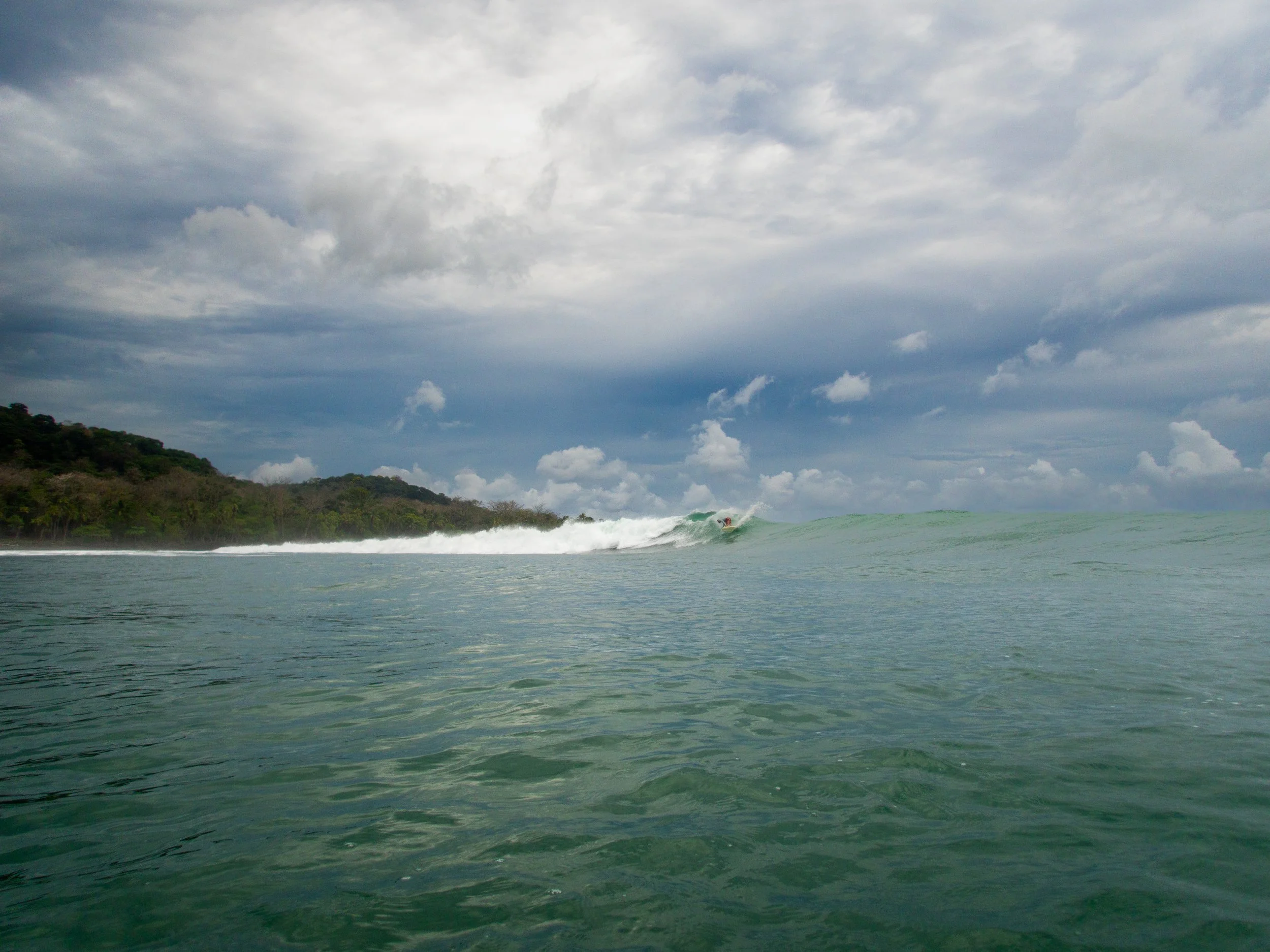 ocean surfing scene with cloudy sky and green hills
