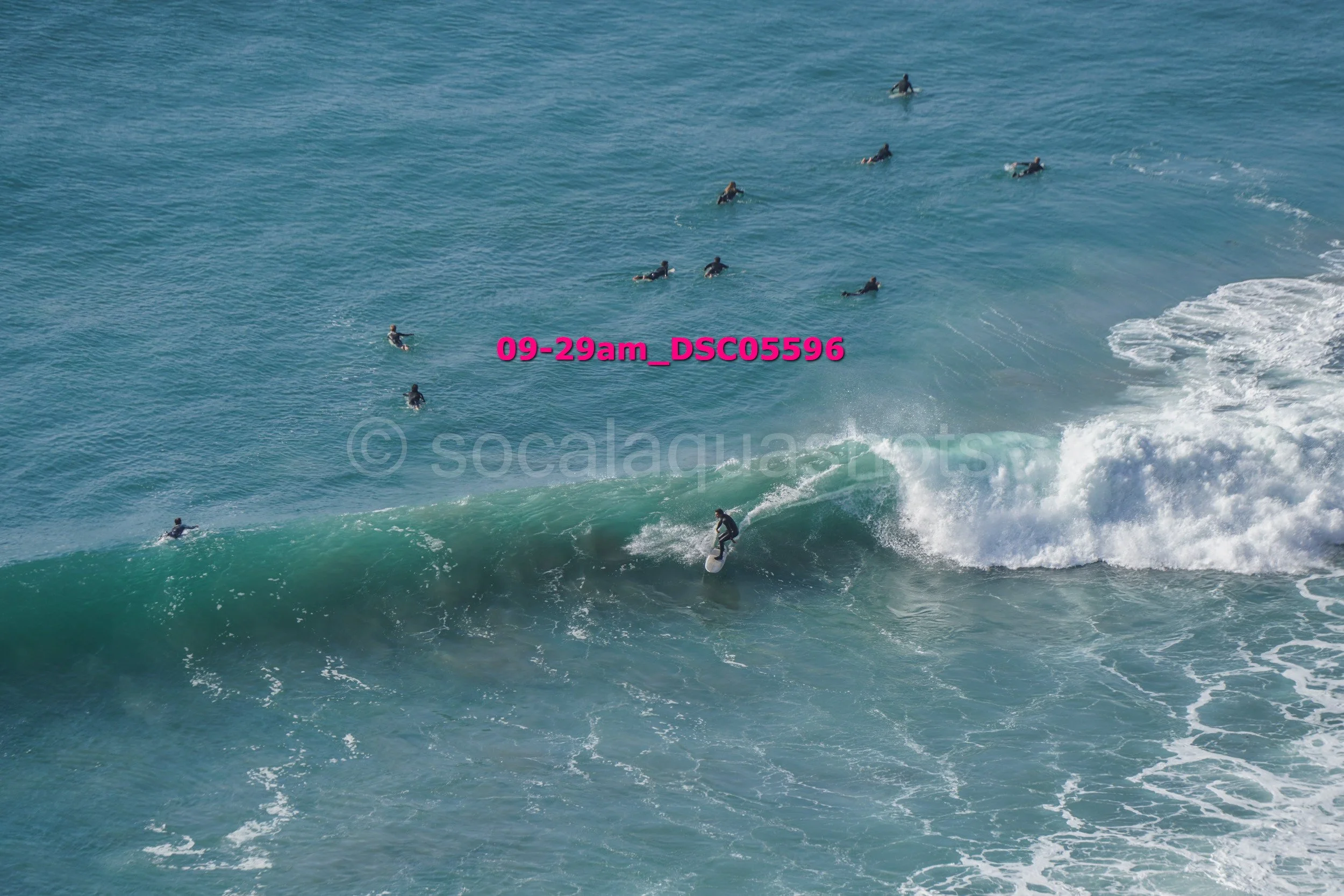 A surfer riding a wave with multiple surfers and swimmers in the ocean around him.