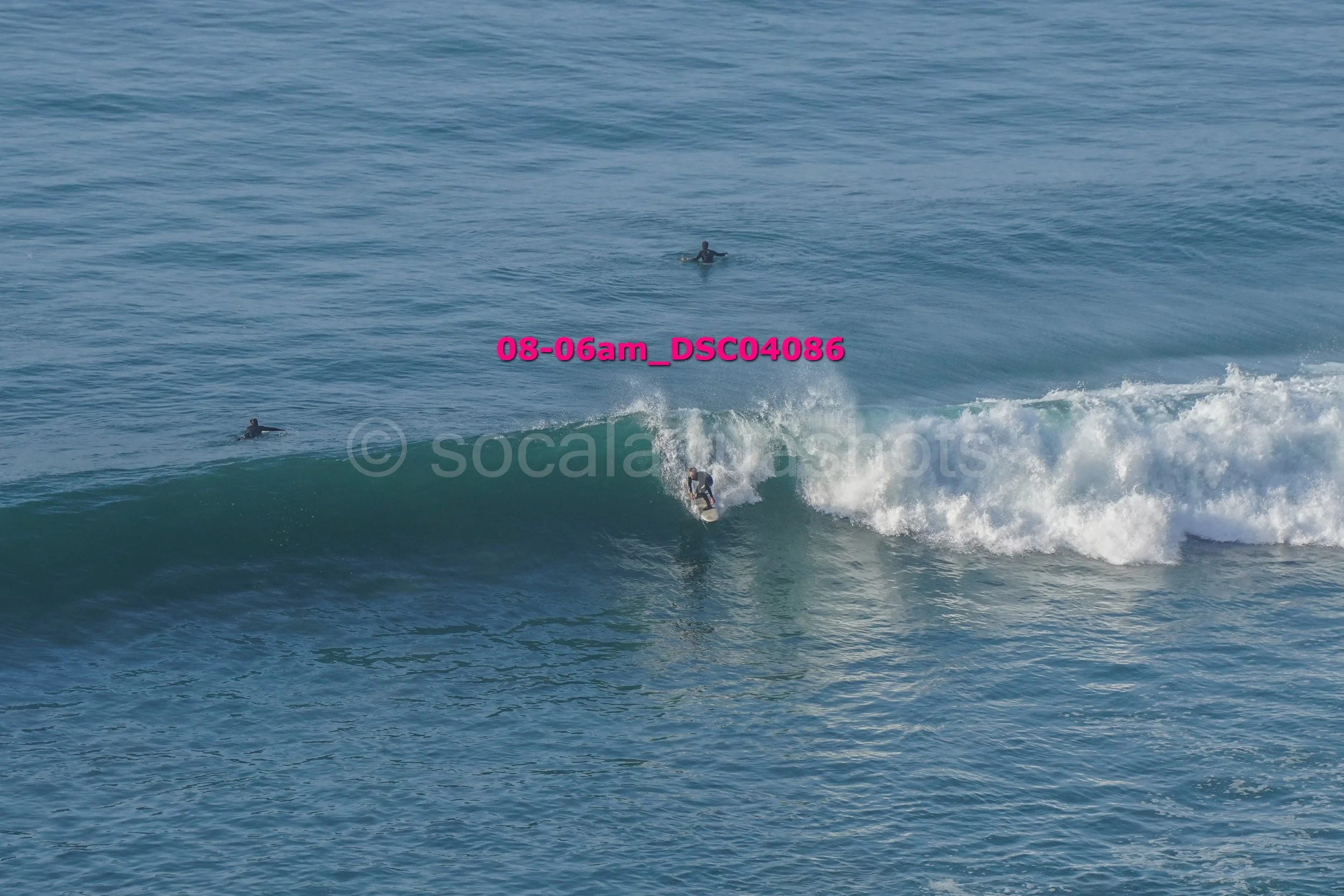 A person surfing on a wave in the ocean, with two other people in the water watching from a distance.