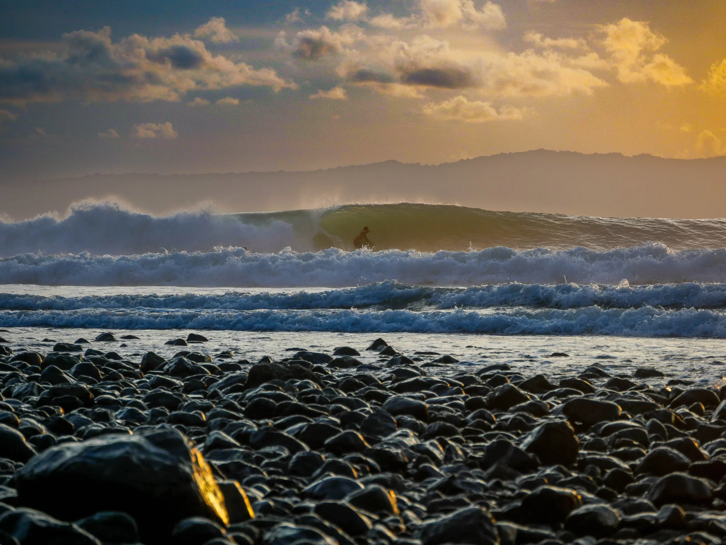 Surfer riding wave during sunset near rocky shore