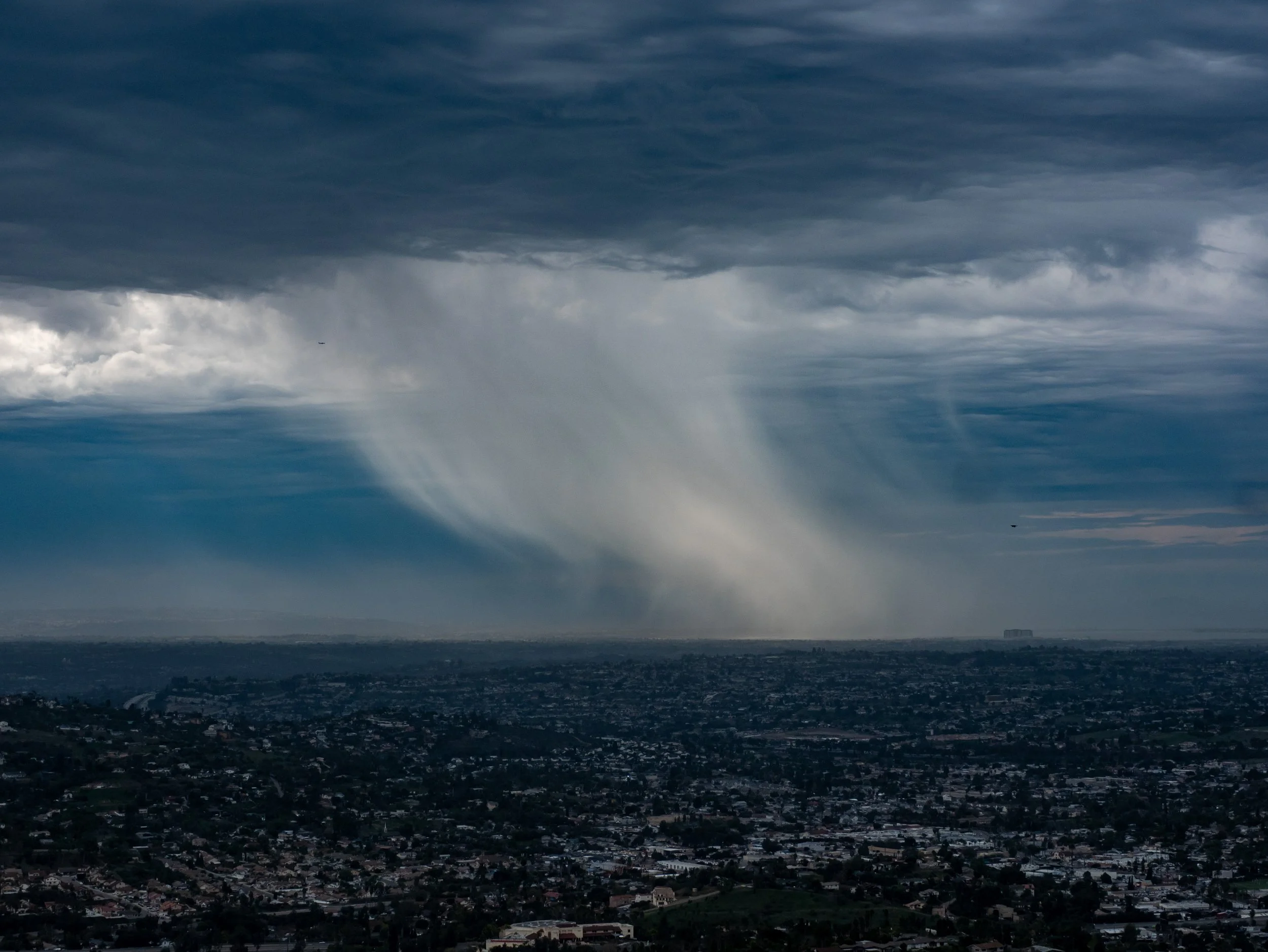 Dark storm cloud over a city with rain falling in the distance, under a dark and cloudy sky.