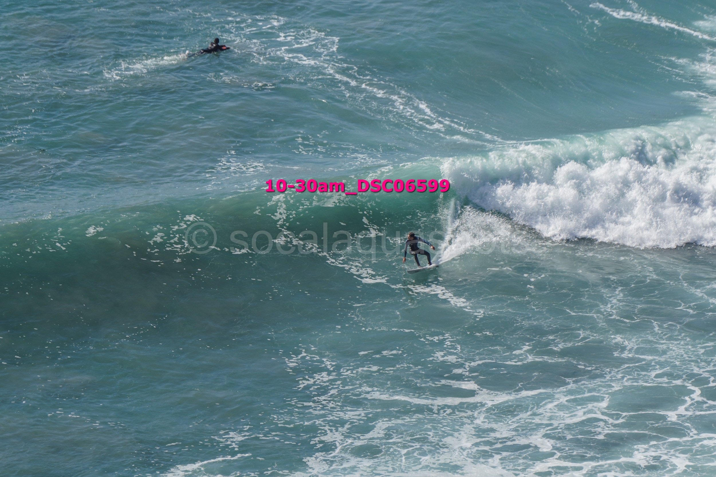 A person surfing on a large wave in the ocean, with another person in the water nearby.