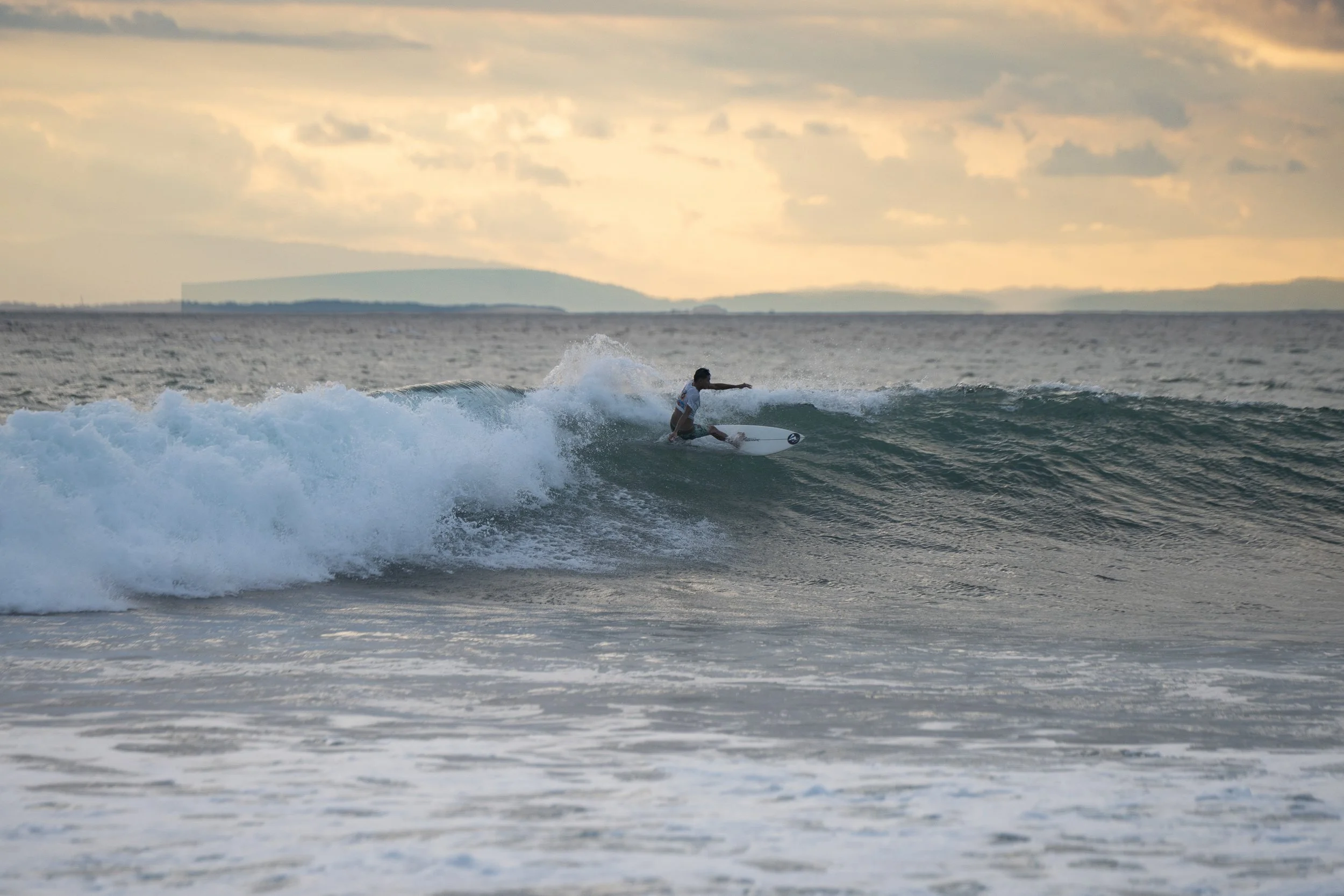 Person surfing on a wave in the ocean during sunset.