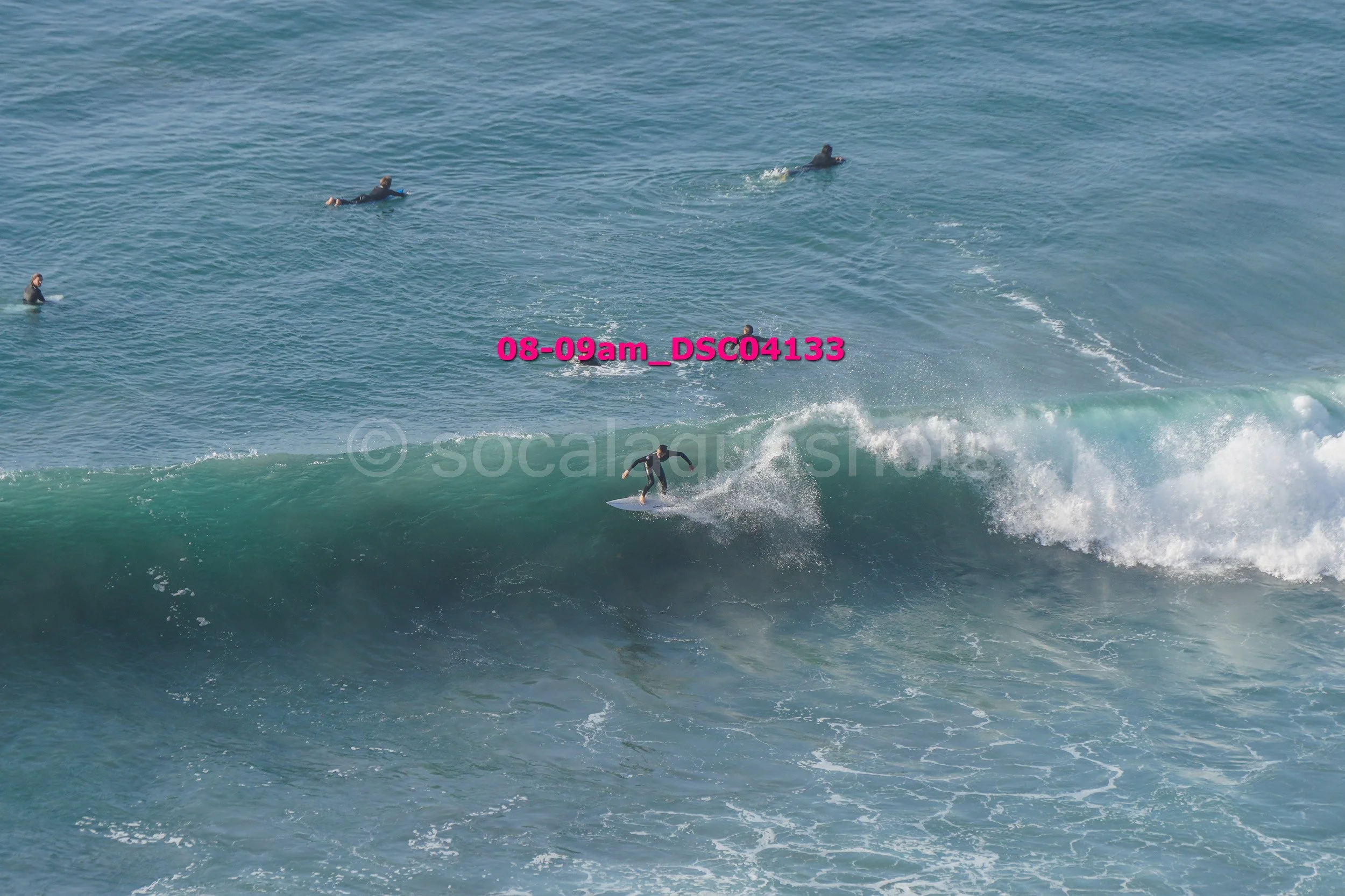 A surfer riding a wave with several people in the water watching from behind.