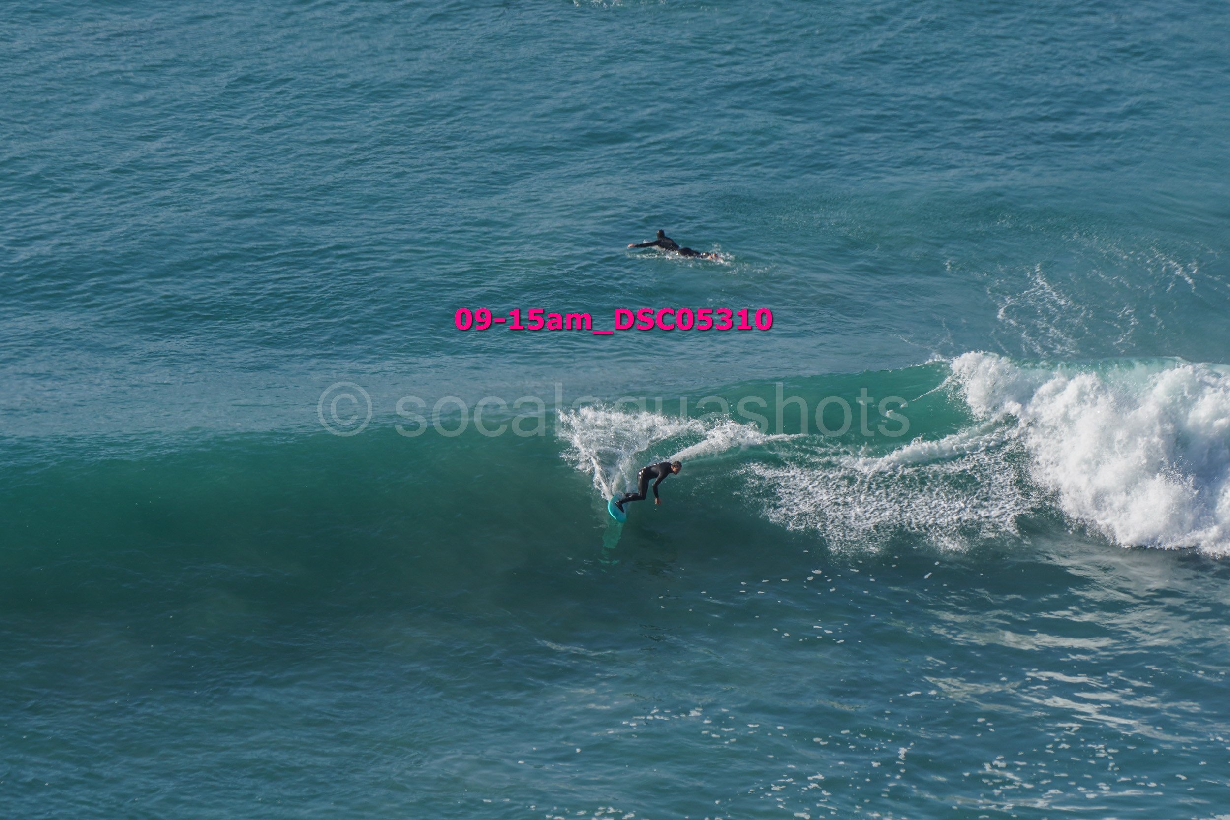 A person surfing on a wave in the ocean with another person swimming in the background.