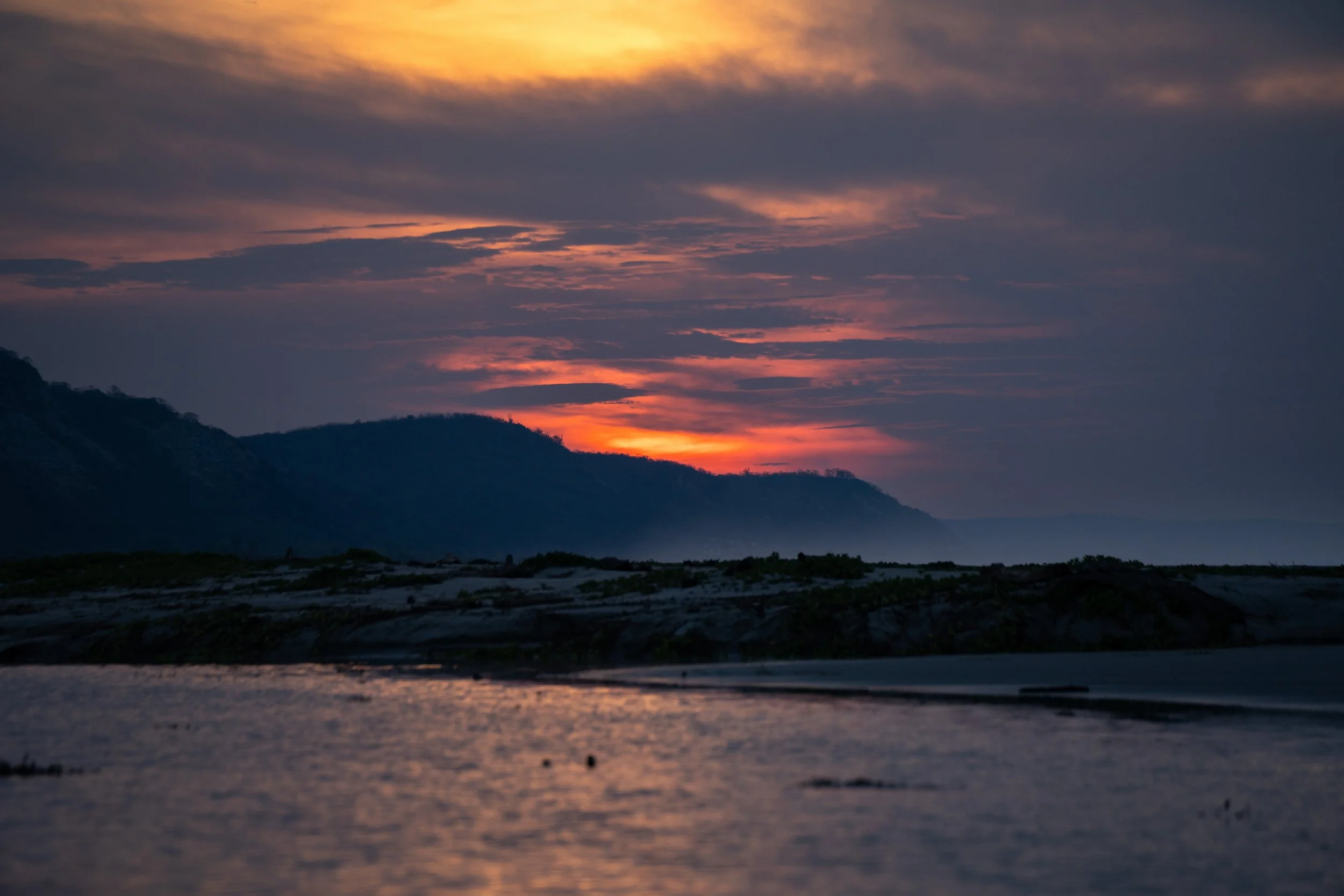 A scenic view of a colorful sunset over a mountainous landscape with water in the foreground.