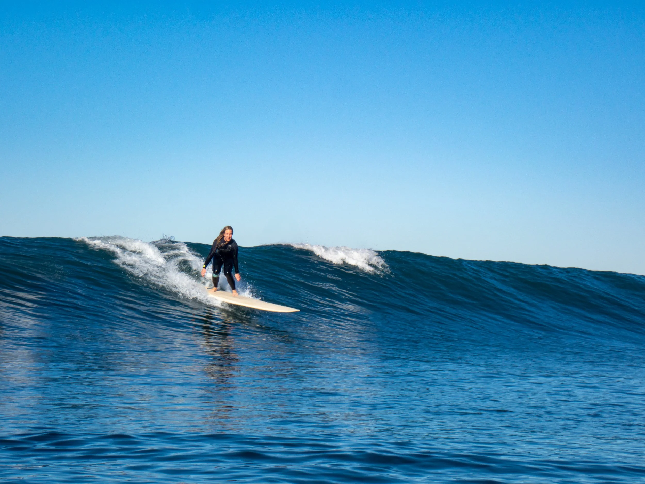 Person surfing on a wave in the ocean under a clear blue sky.