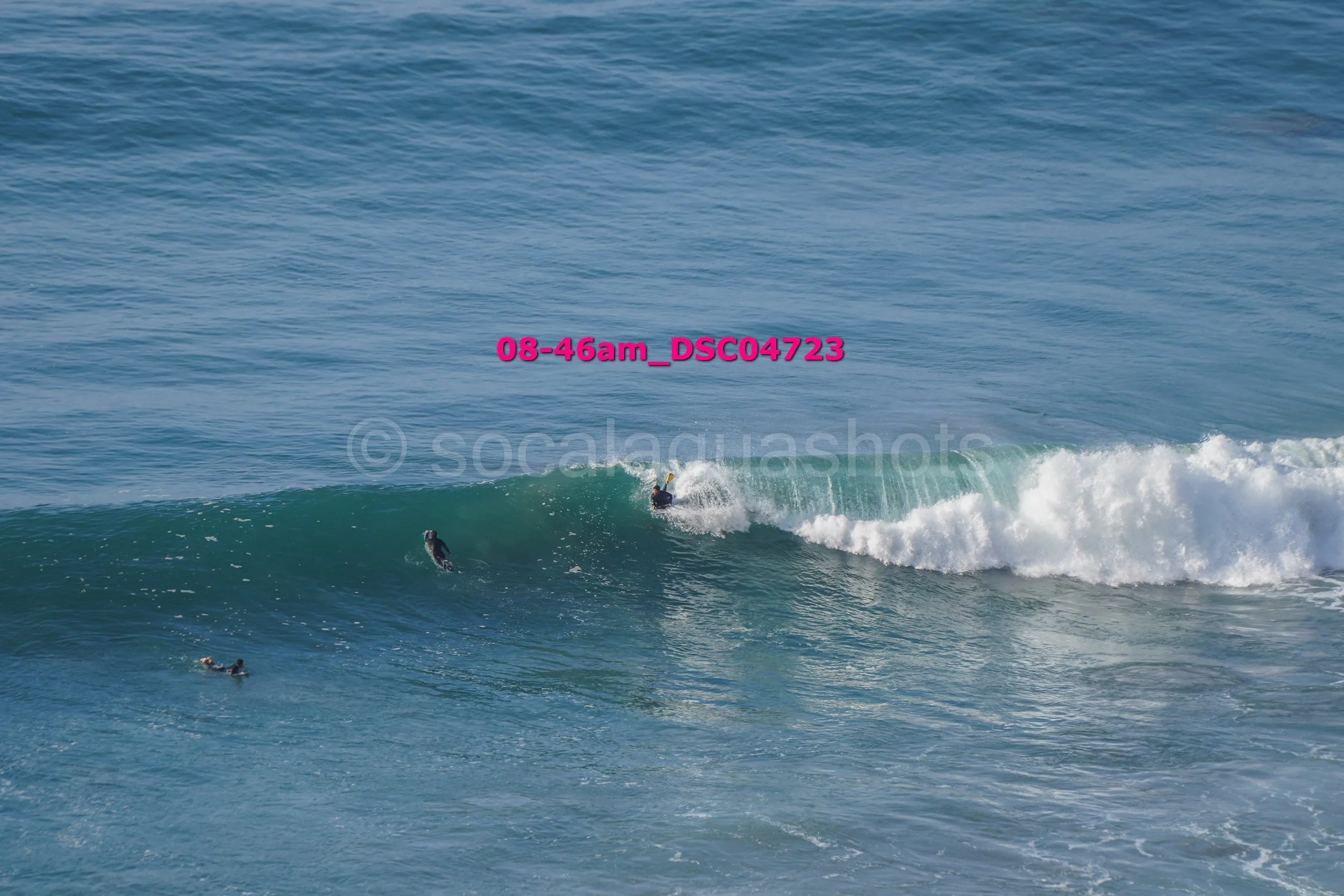 Beach scene with surfers riding a wave in the ocean.