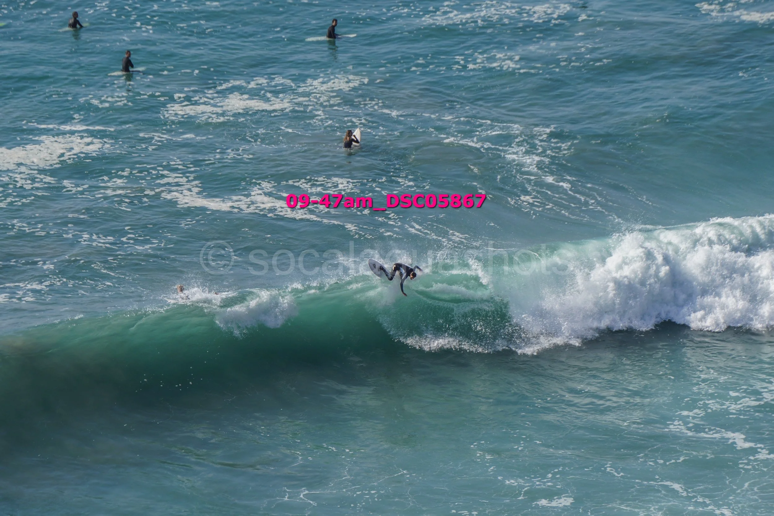 Surfer riding a wave with several people in the water nearby.