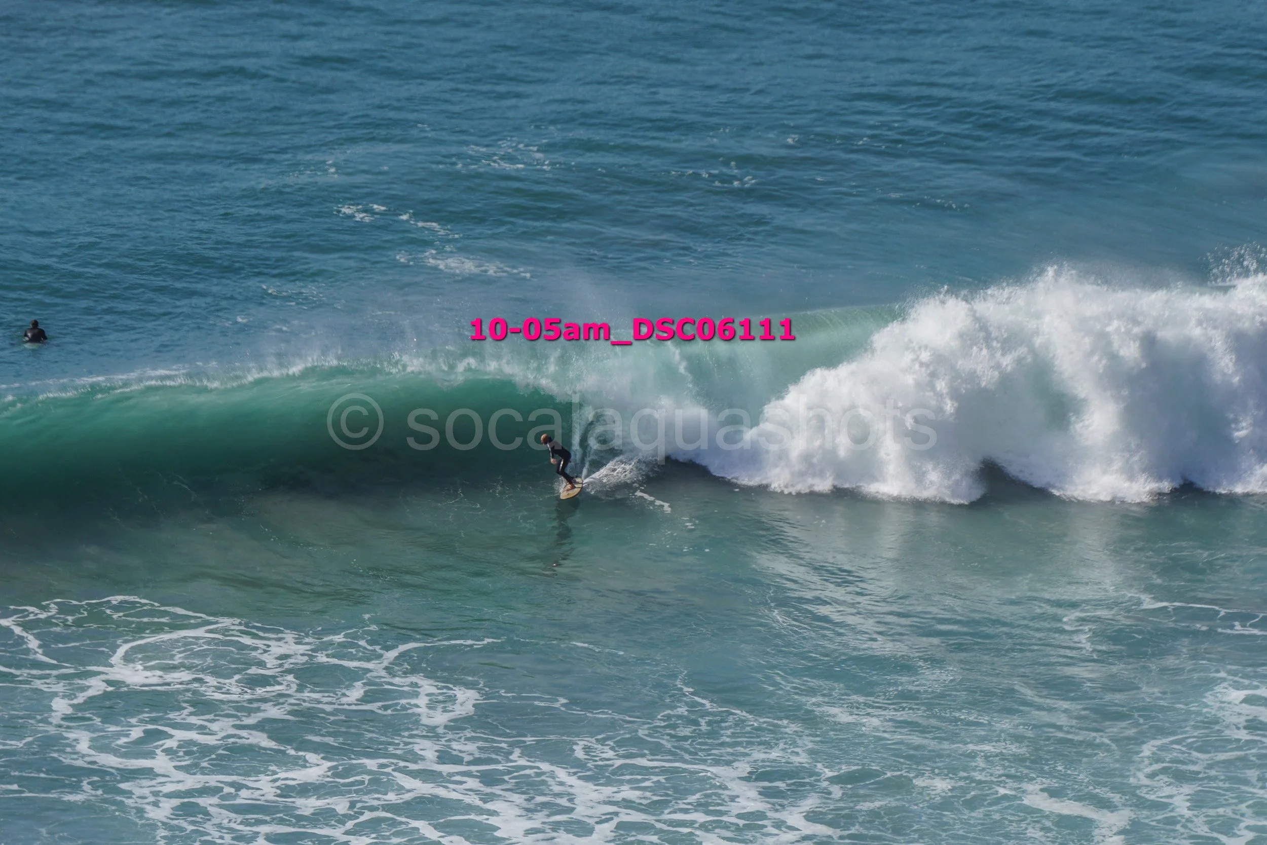 A person surfing on a large wave in the ocean with another surfer in the background.