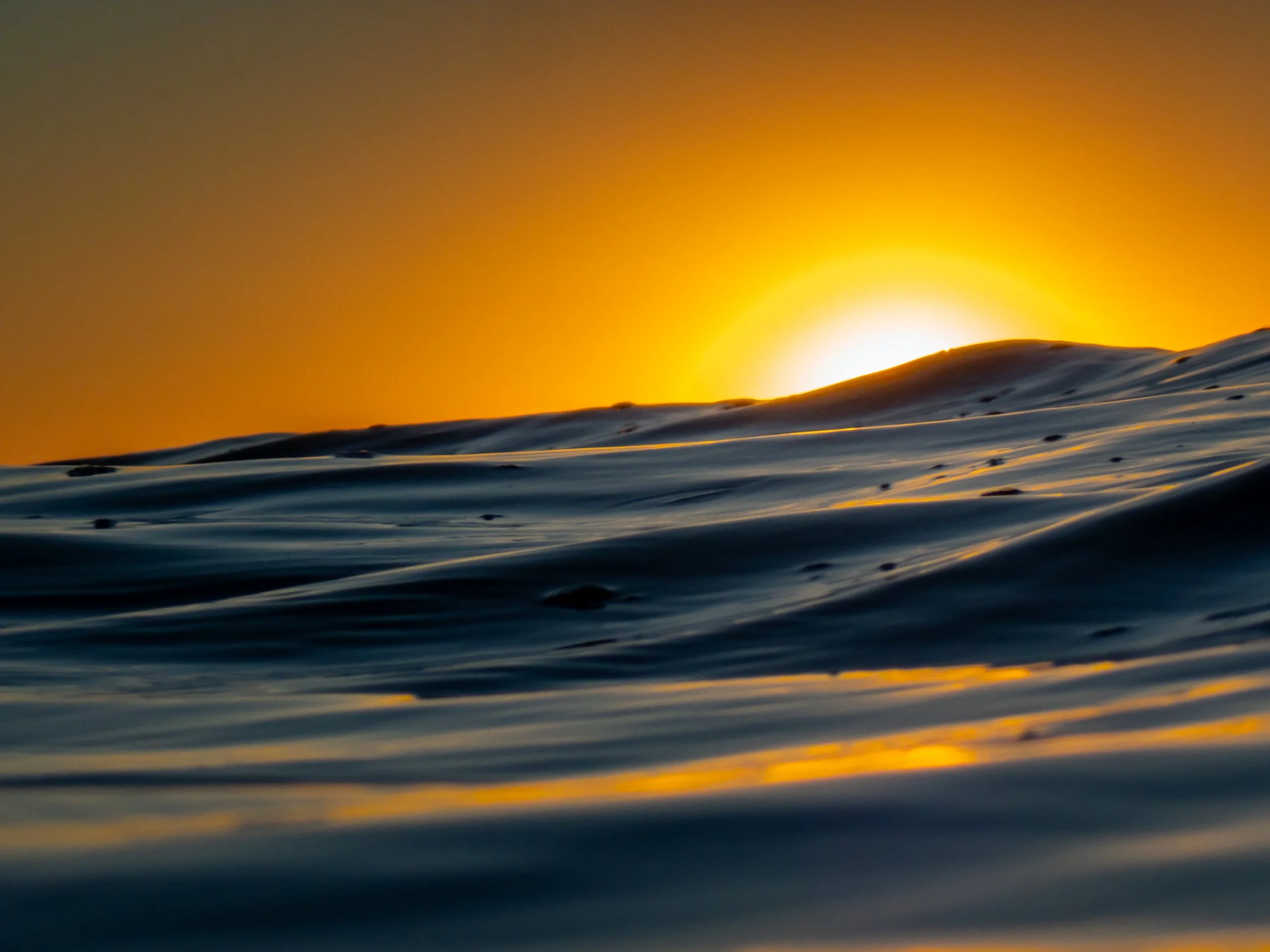 Sunset over calm ocean waves with orange sky.