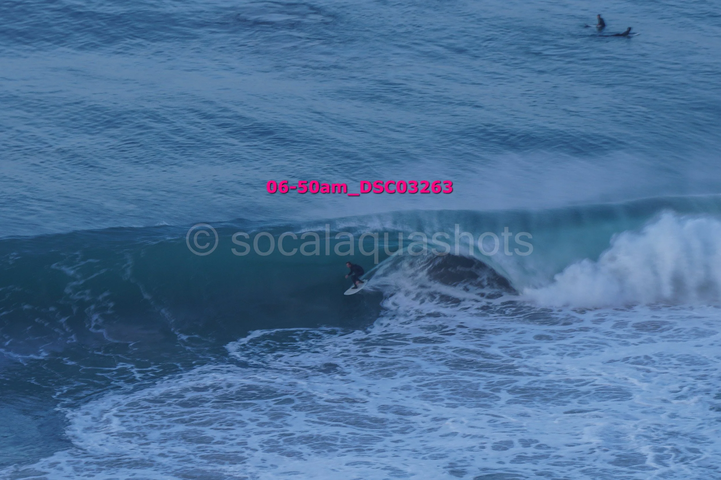 A surfer riding a wave in the ocean with two other surfers visible in the water in the distance.