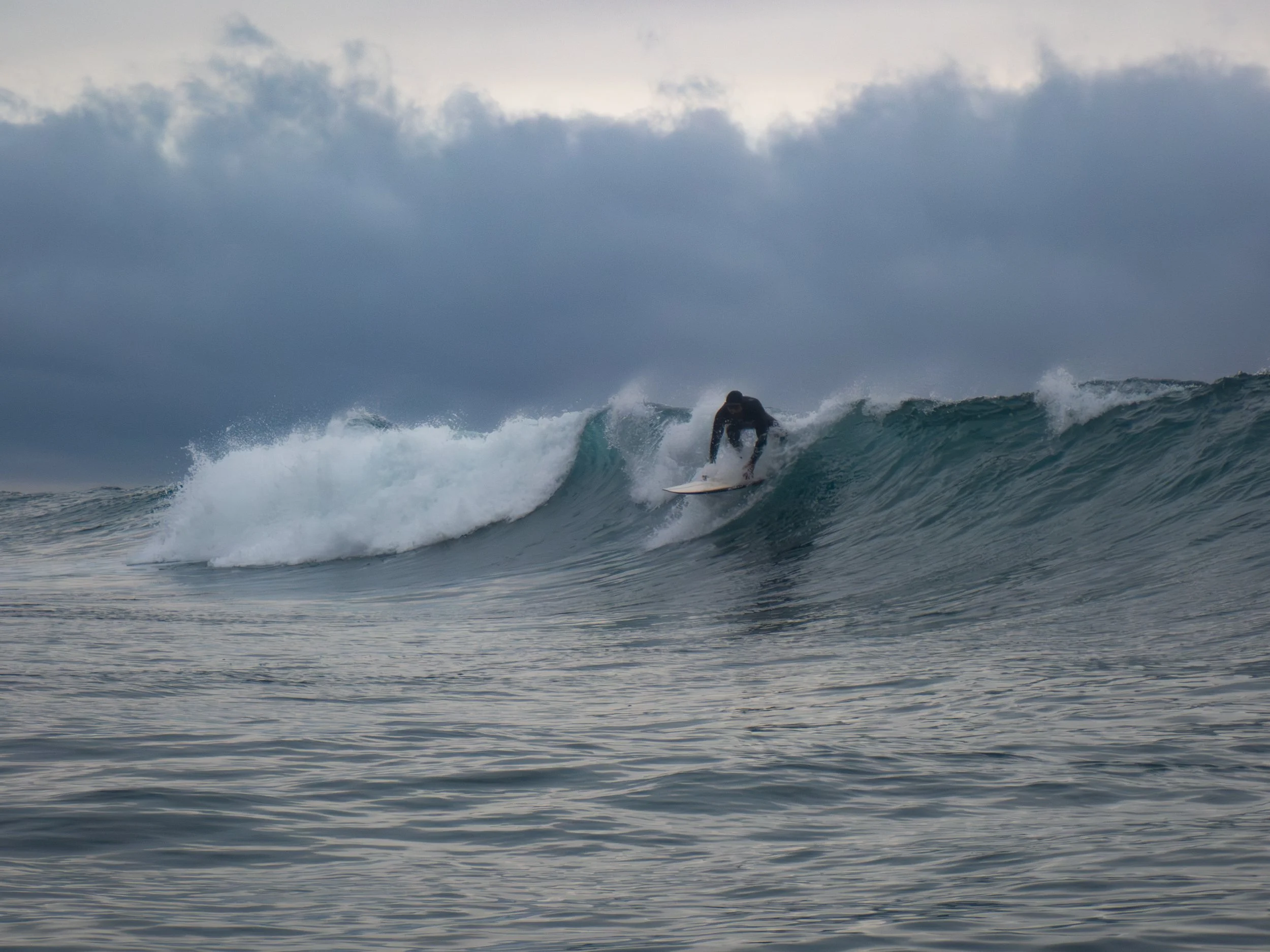 A person surfing on a wave in the ocean under a cloudy sky.