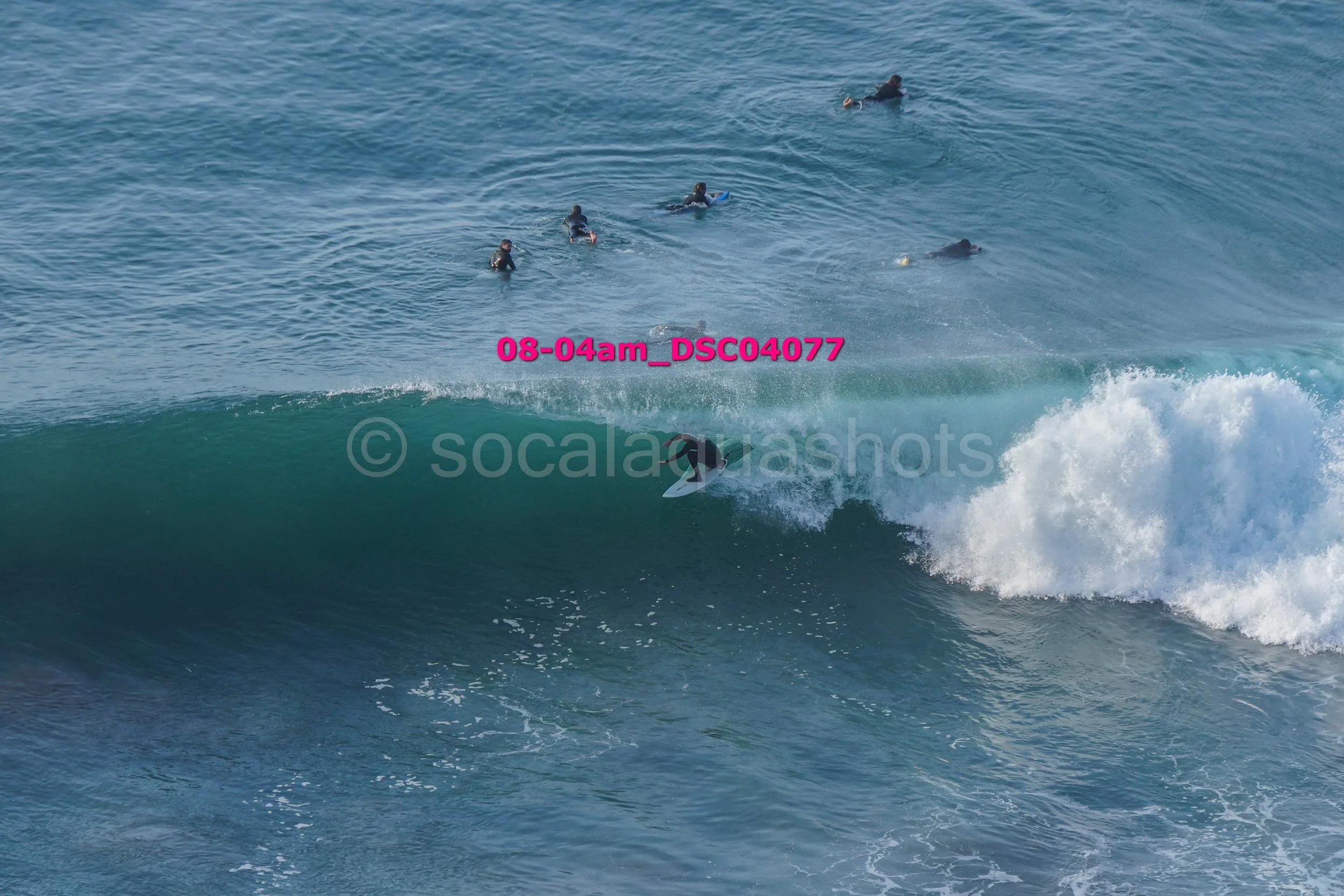 Surfer riding a wave with several people swimming in the background in the ocean.