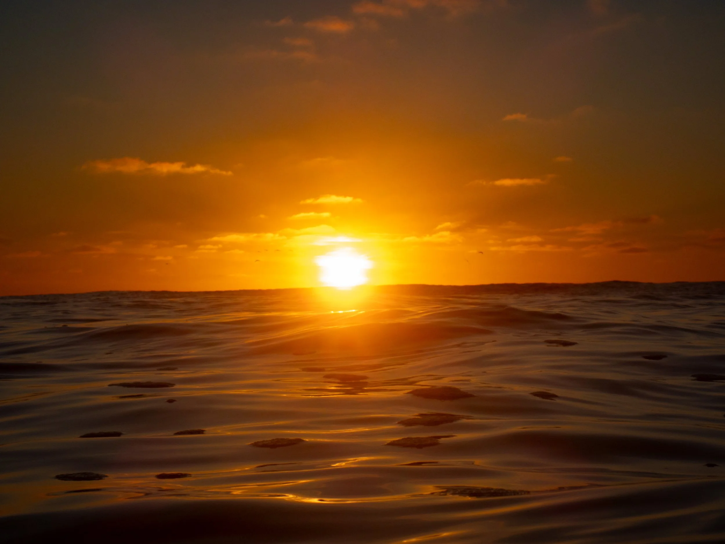 Sunset over the ocean with the sun near the horizon and gentle waves on the water.