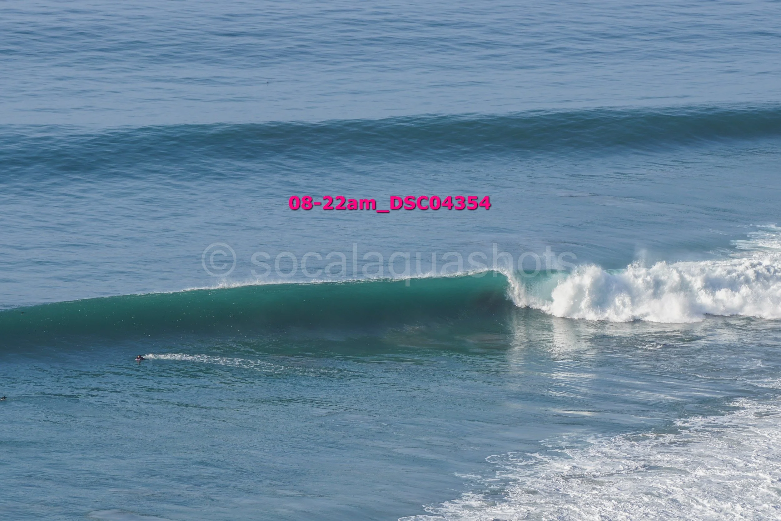 Ocean waves with one surfer riding a wave near the shoreline.