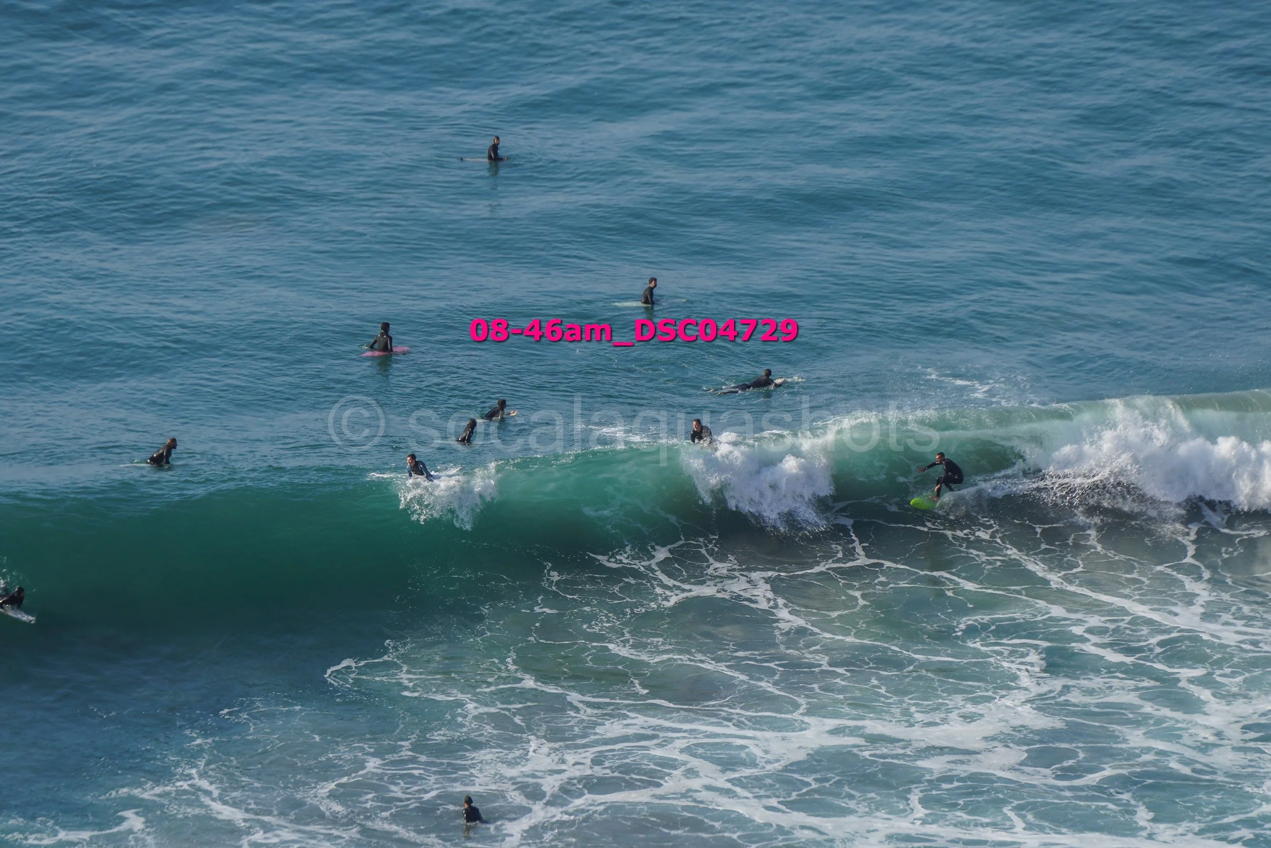 People surfing and swimming in the ocean with one person riding a wave on a surfboard.