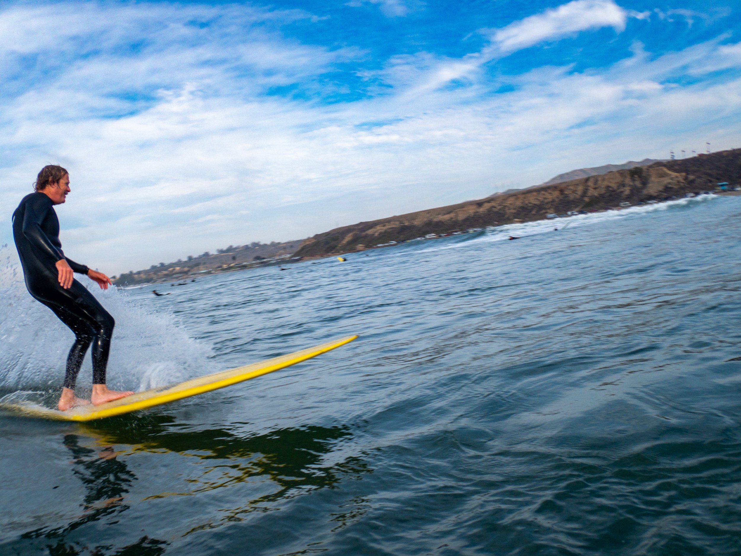 Person surfing on a yellow surfboard in ocean with coastline and hills in background.