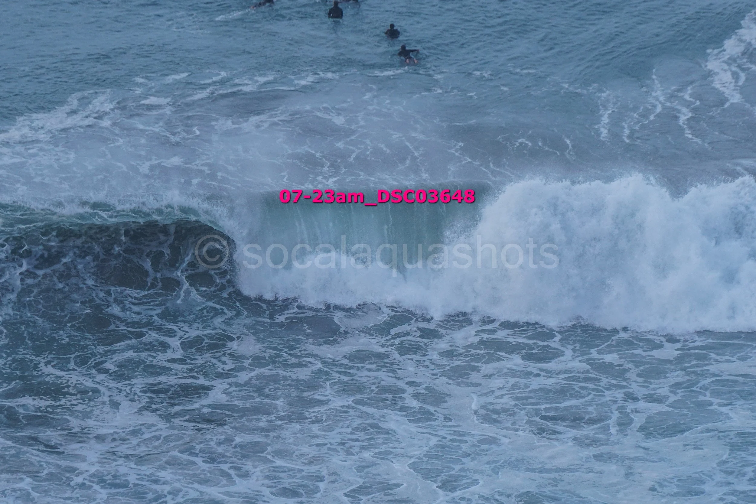 Waves crashing in the ocean with three surfers in the distance