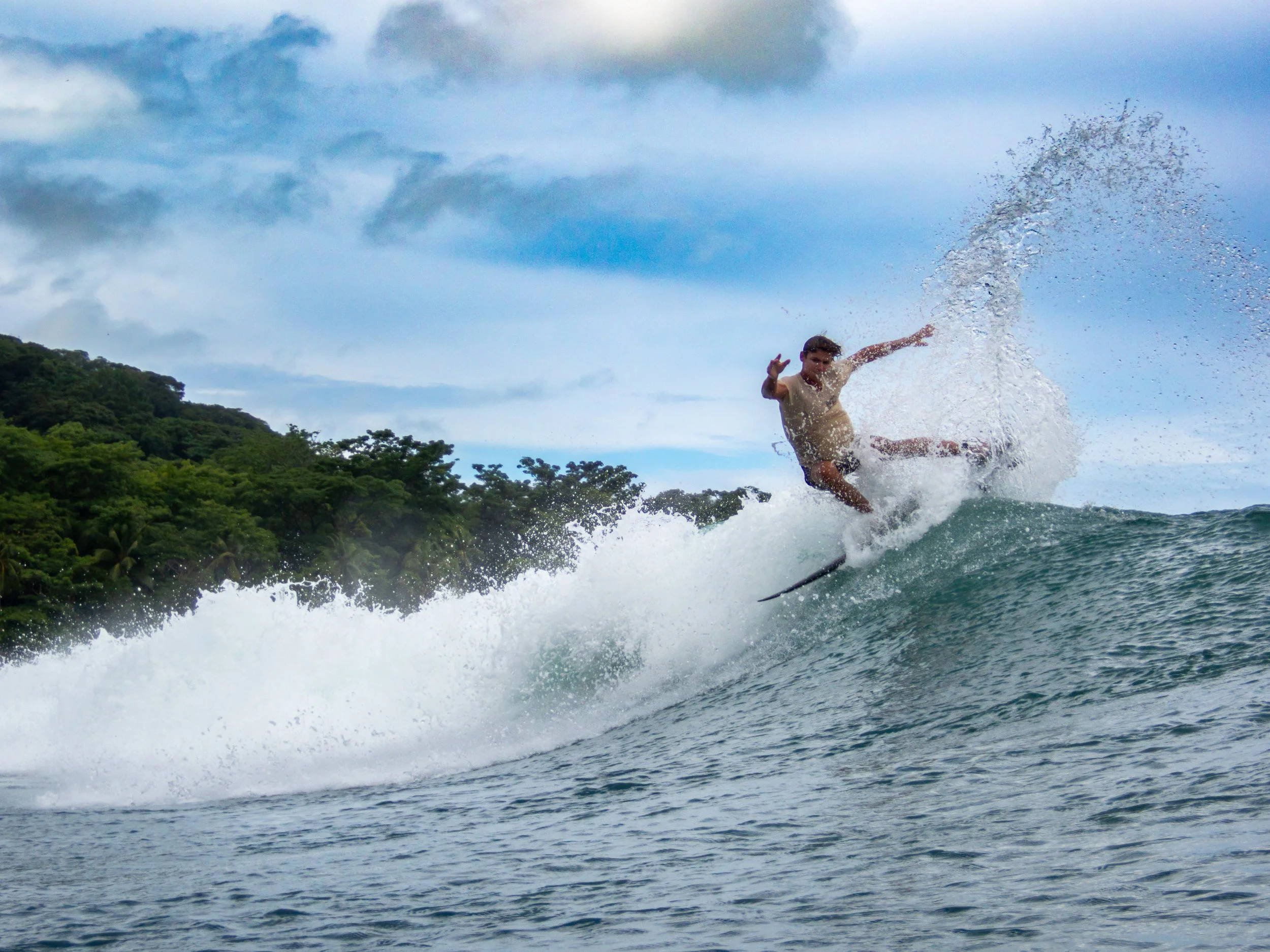 surfer performing trick on wave against forest background