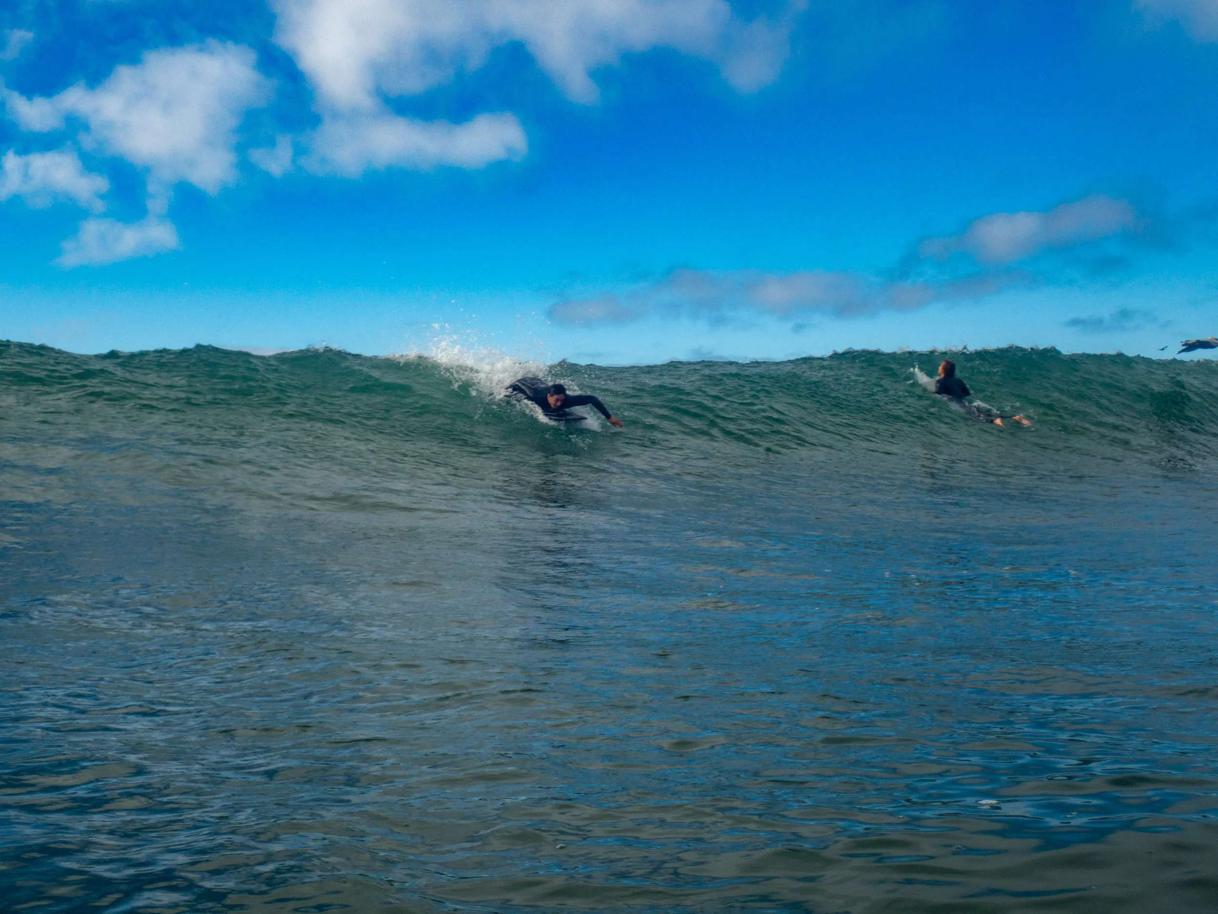 Two surfers riding on waves in the ocean under a blue sky with some clouds.