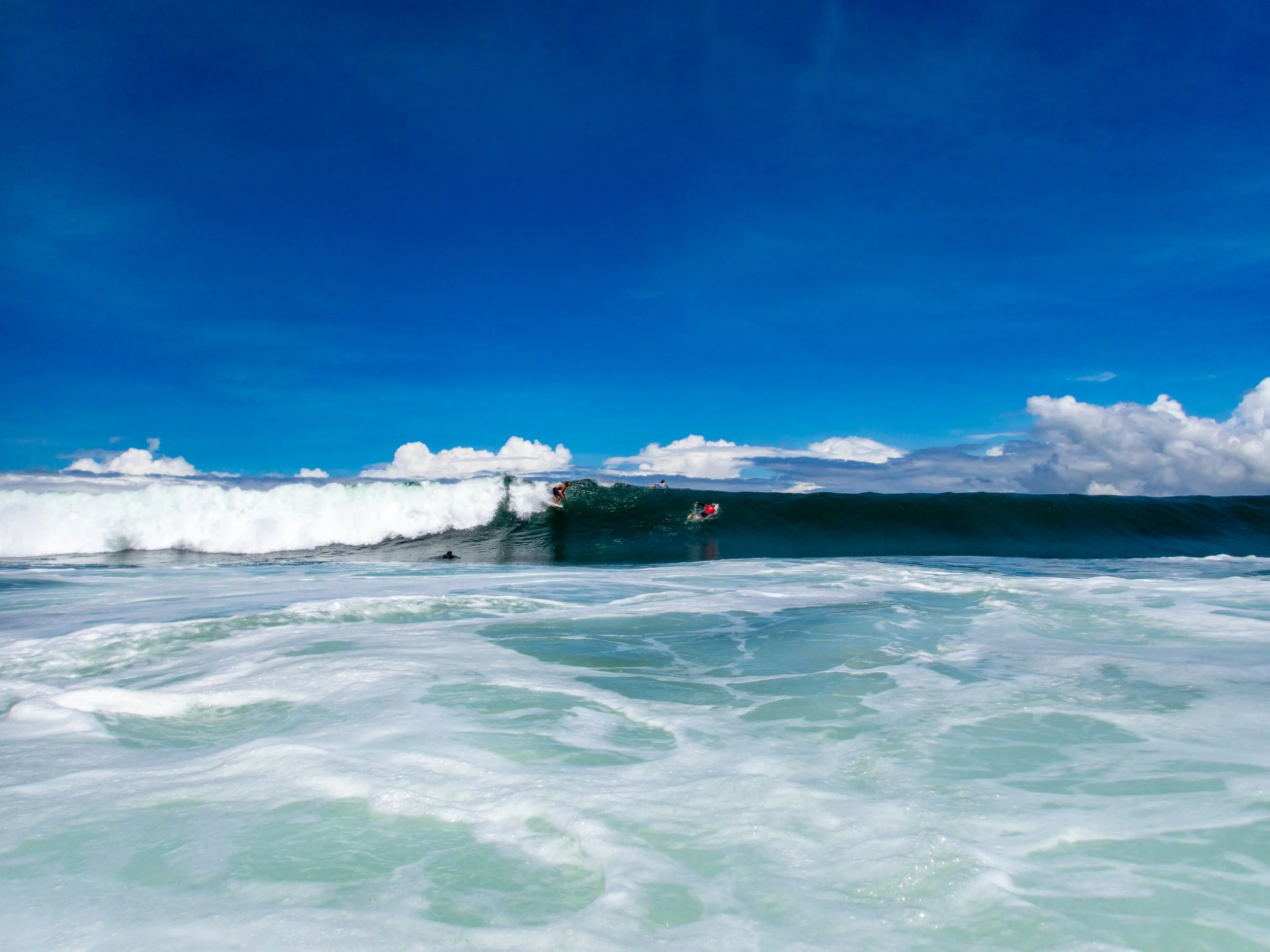 Surfer riding a large ocean wave under a clear blue sky