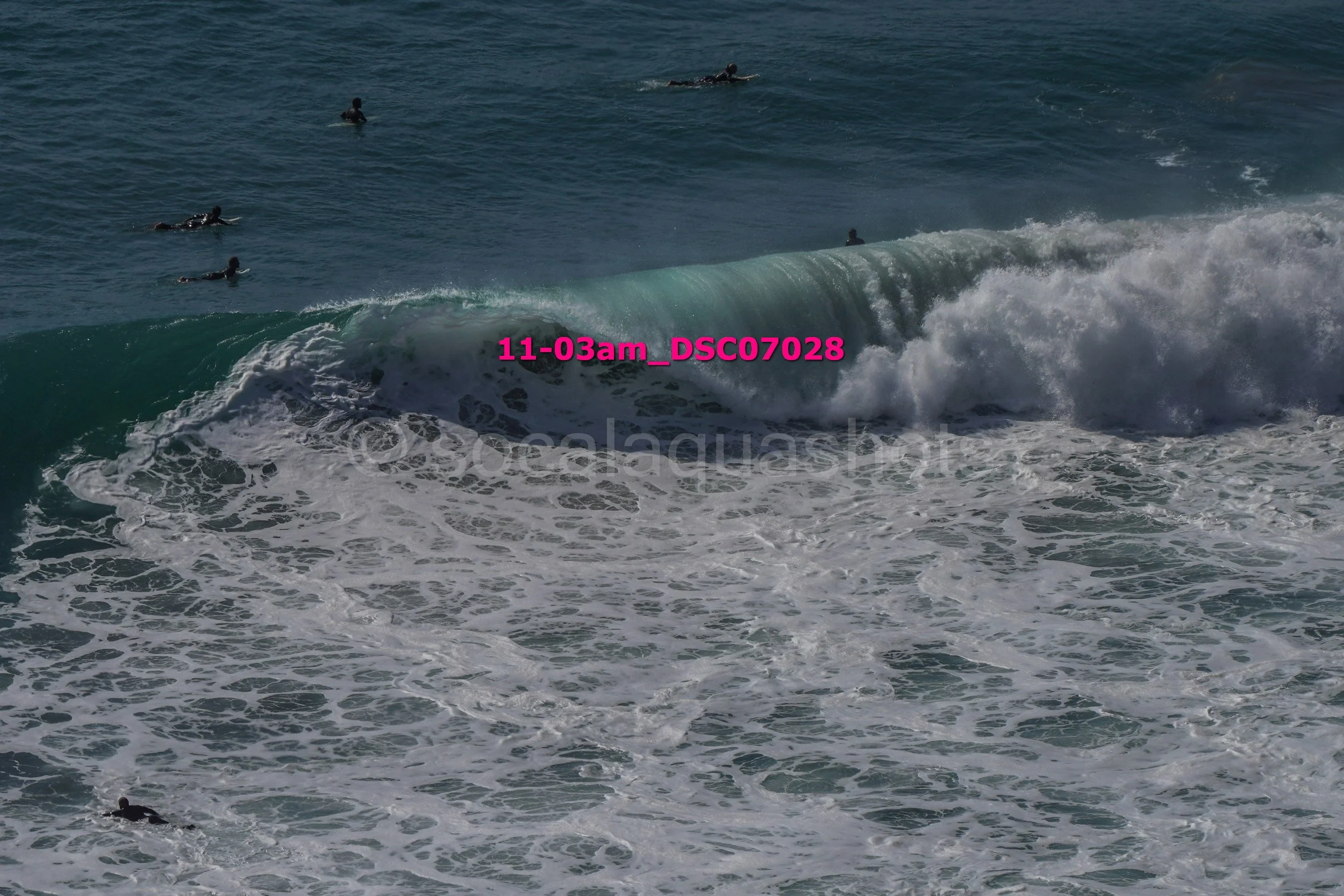 People surfing in the ocean with a large wave approaching.