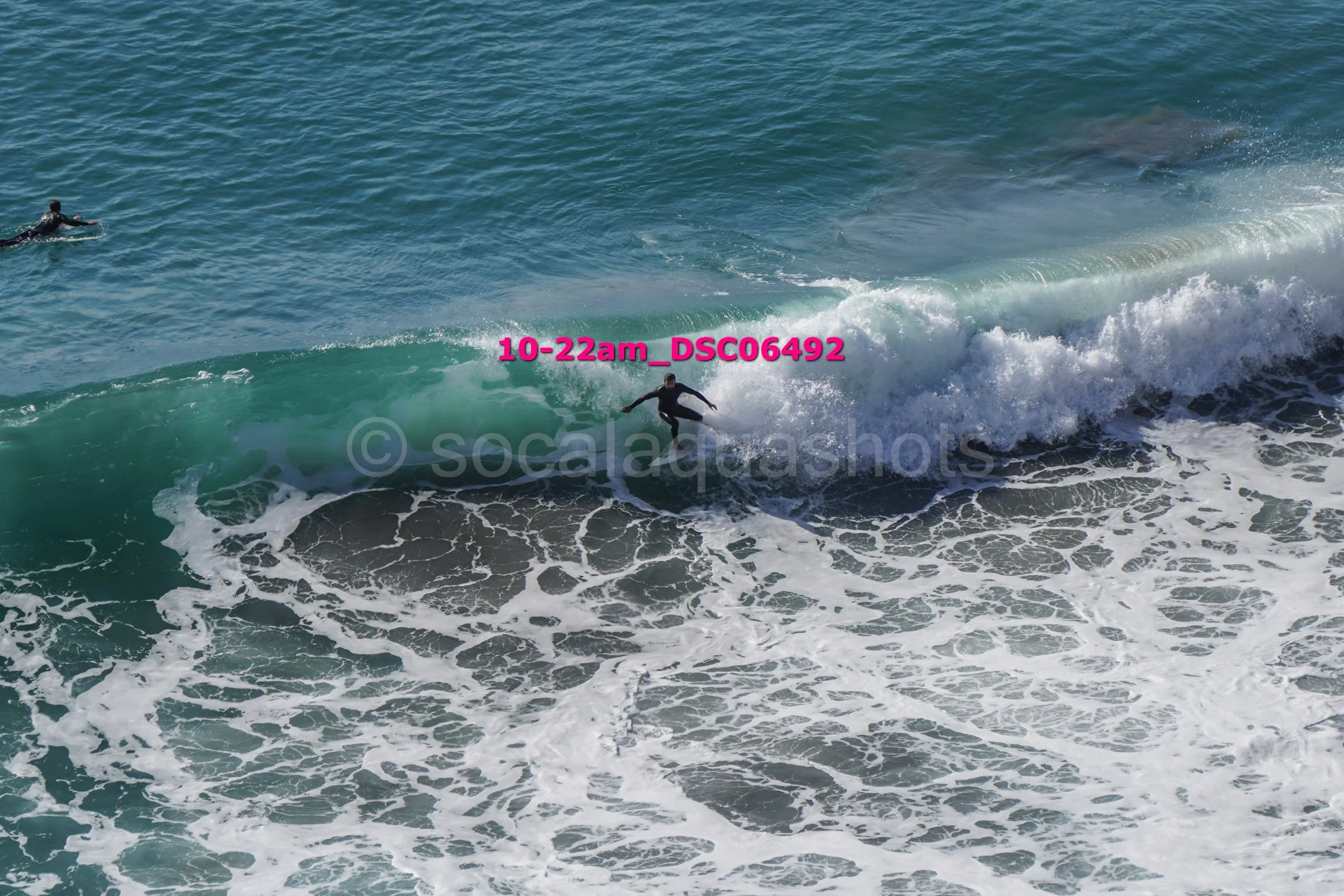 A person surfing on a wave in the ocean, with another surfer in the background.