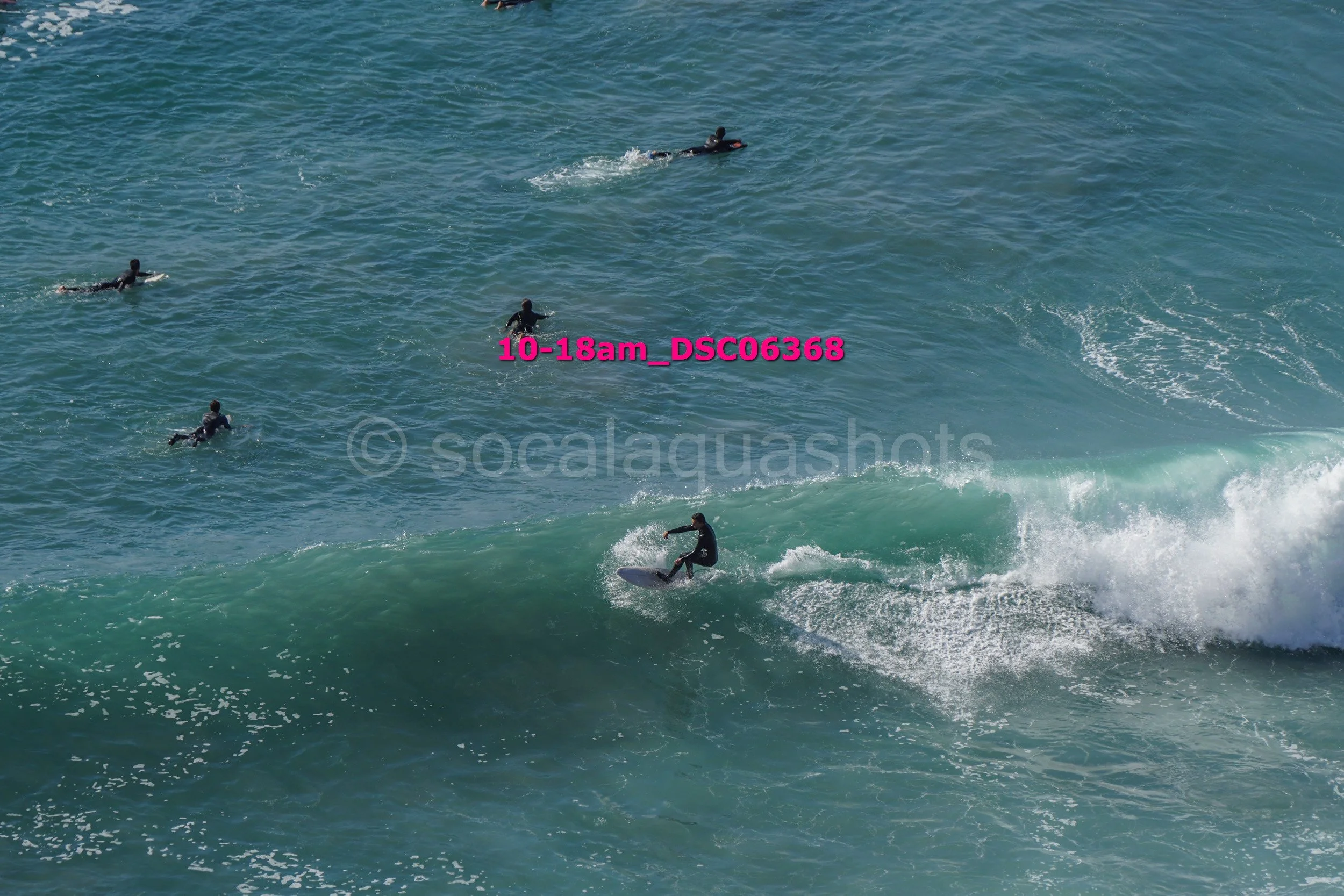 Surfer riding a wave with four surfers paddling in the distance in the ocean.