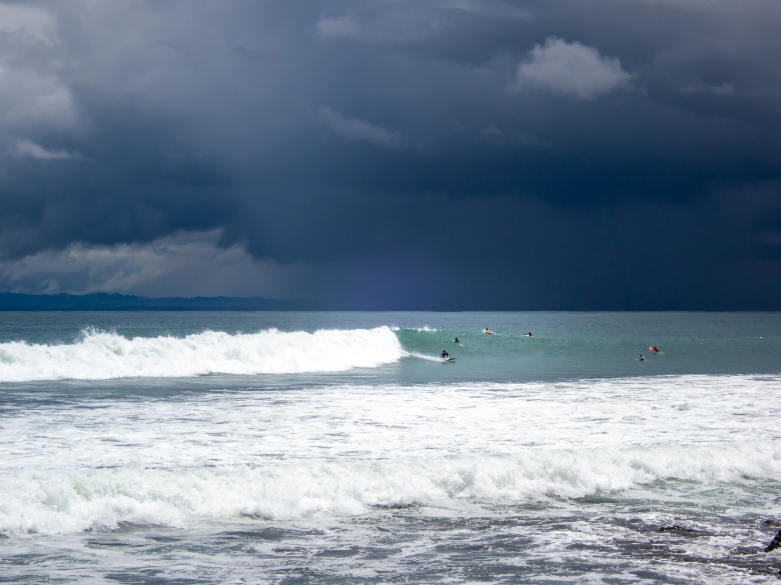 Surfers riding waves with dark storm clouds in the background.